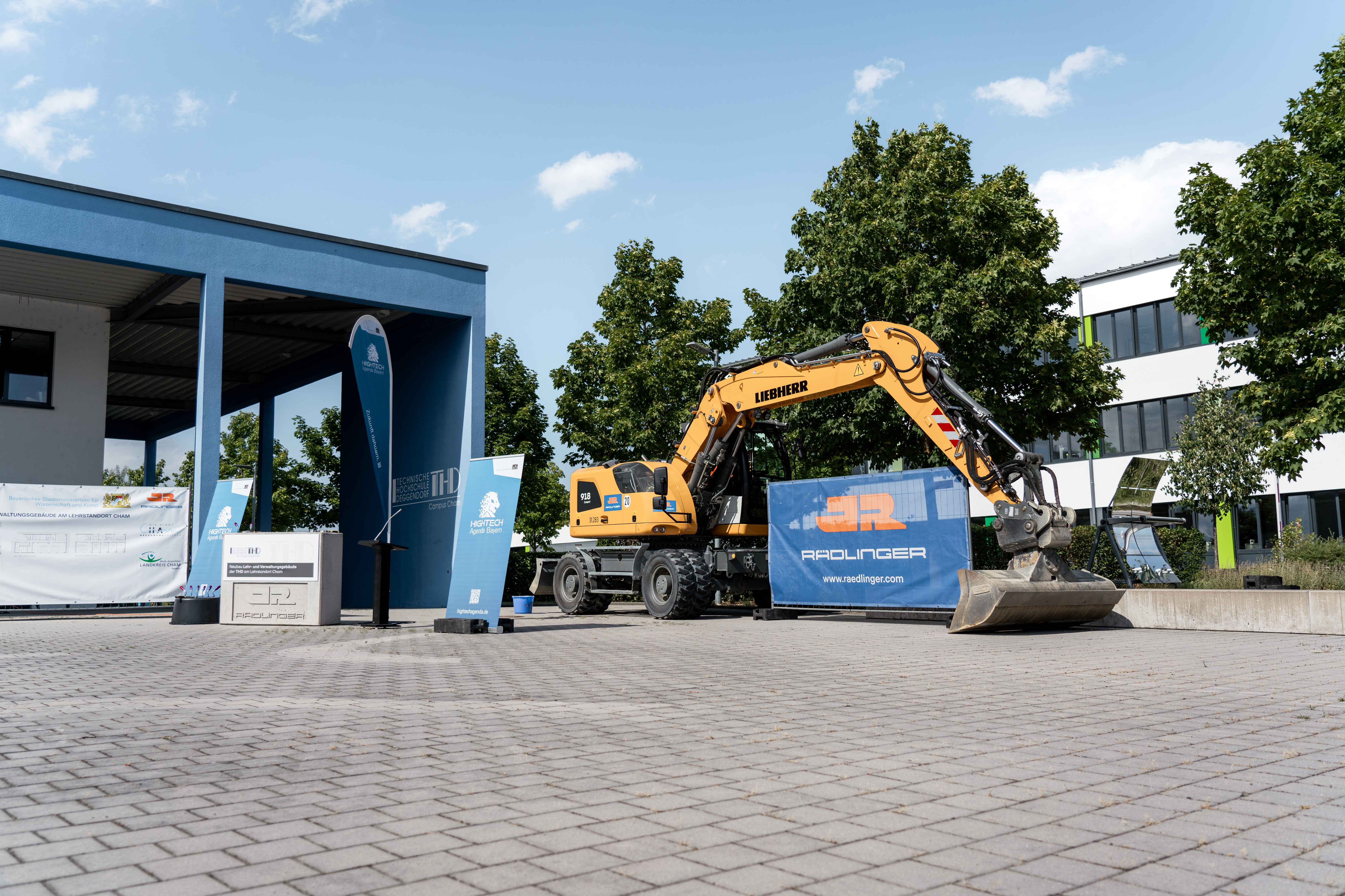 Ein Bagger der Firma JR Rädlinger steht symbolisch auf dem Gelände des künftigen Neubaus