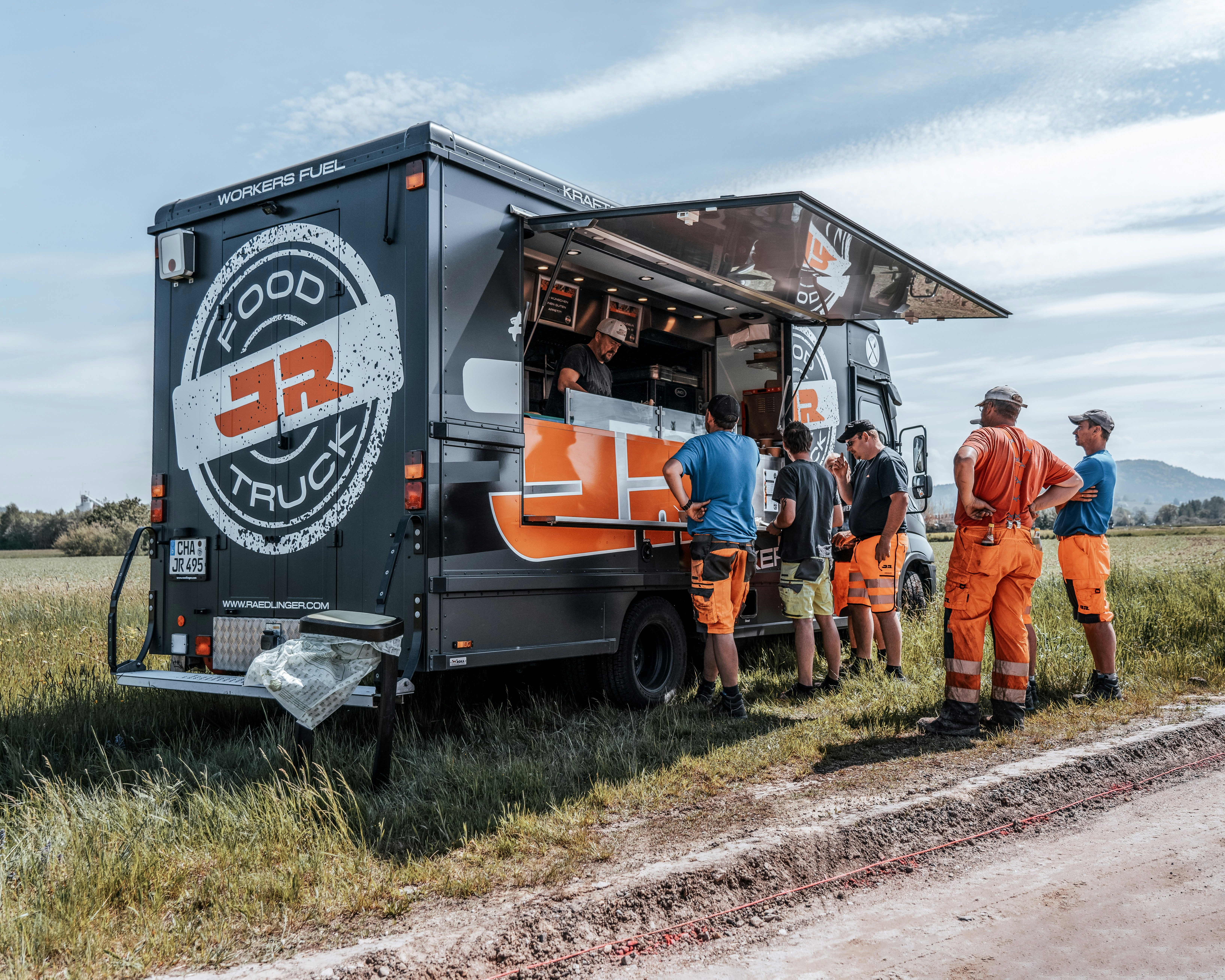 Bauarbeiter bei der Essensausgabe am schwarzen JR Footruck auf der Baustelle