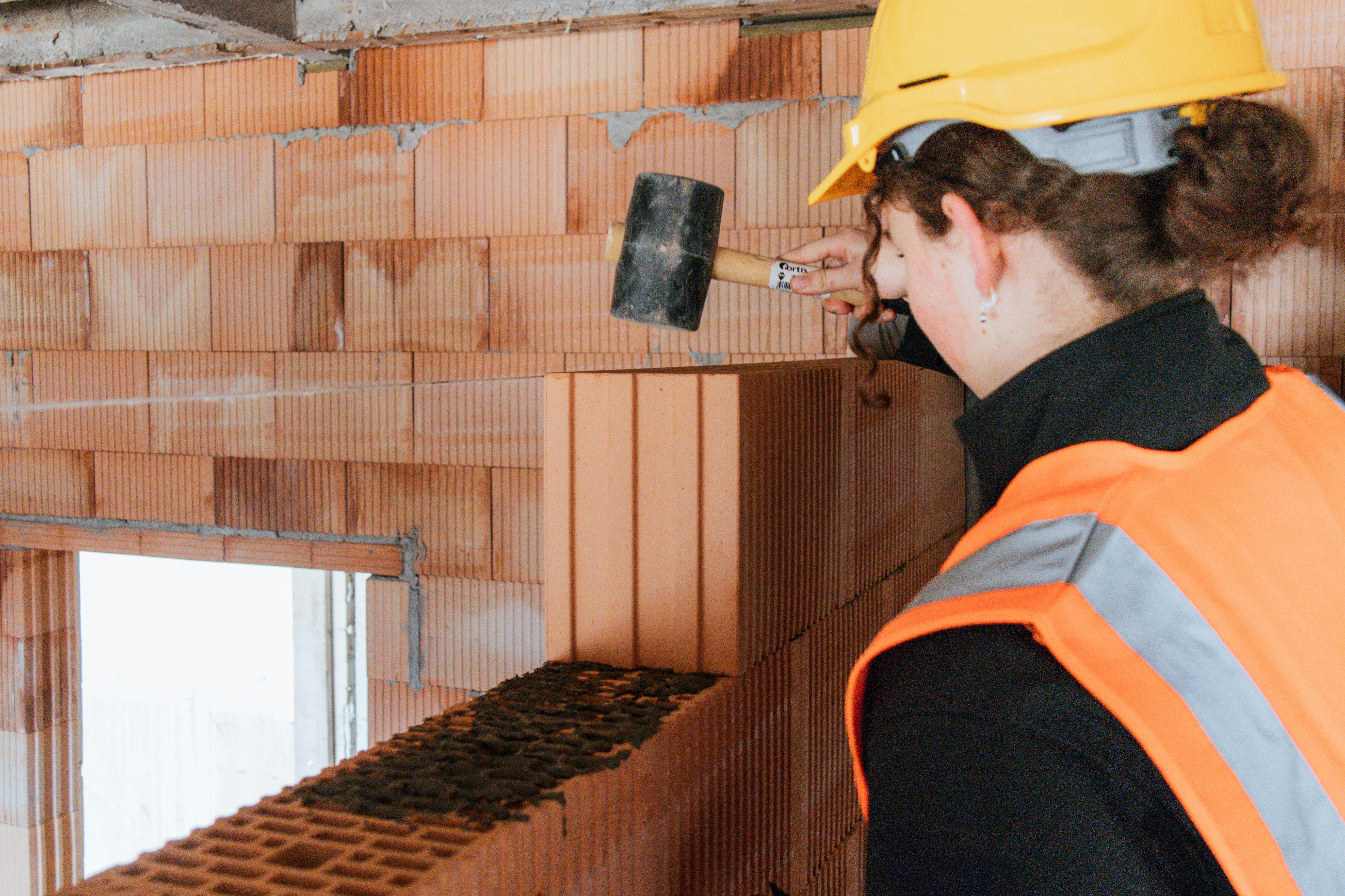 Girls'Day 2025 bei JR: Teilnehmerin befestigt beim Mauern einer Wand mit Gummihammer einen Ziegelstein