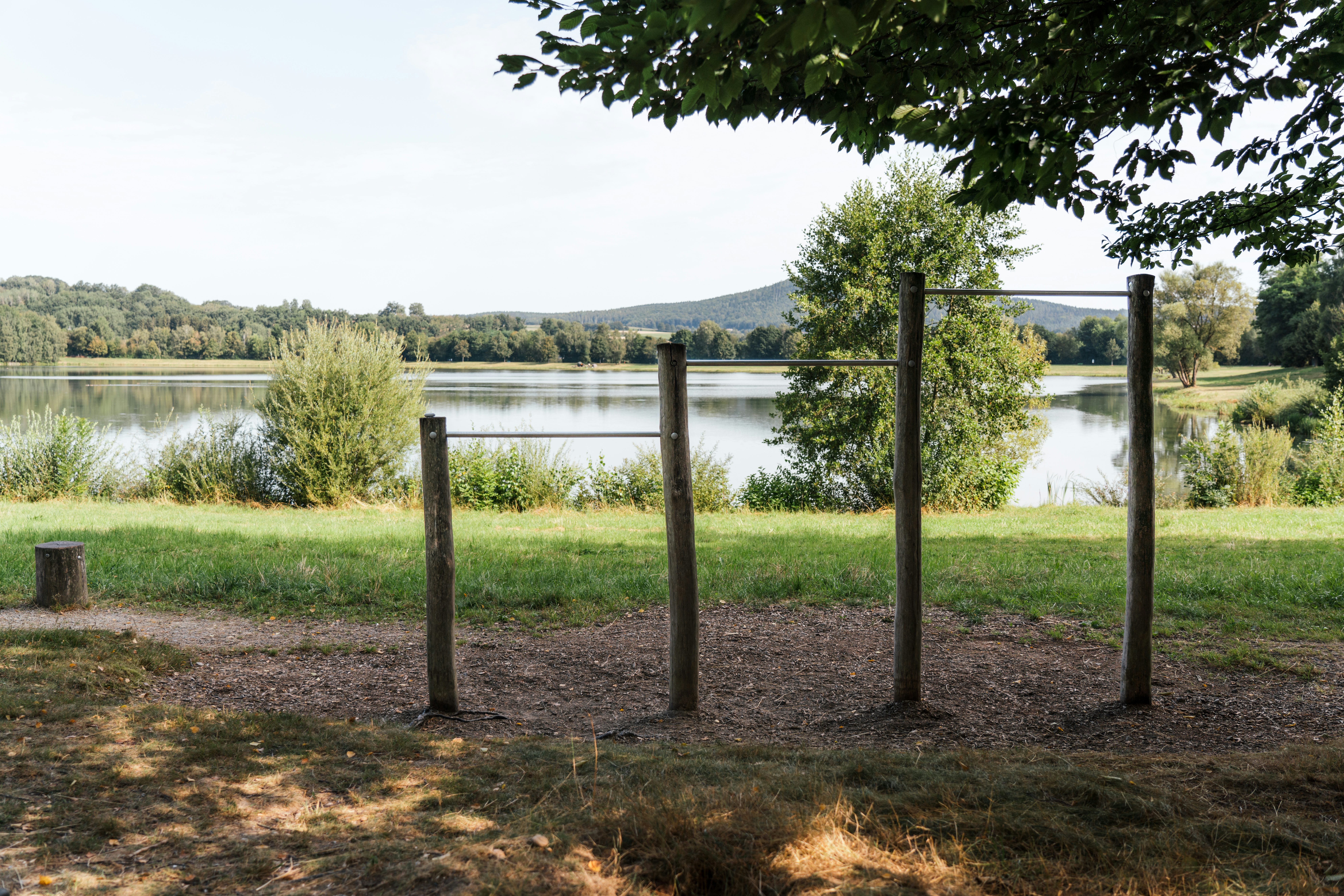Platz der Bewegung am Satzdorfer See: Outdoor-Fitnessgerät aus Holz und Metall am Seeufer, umgeben von Natur