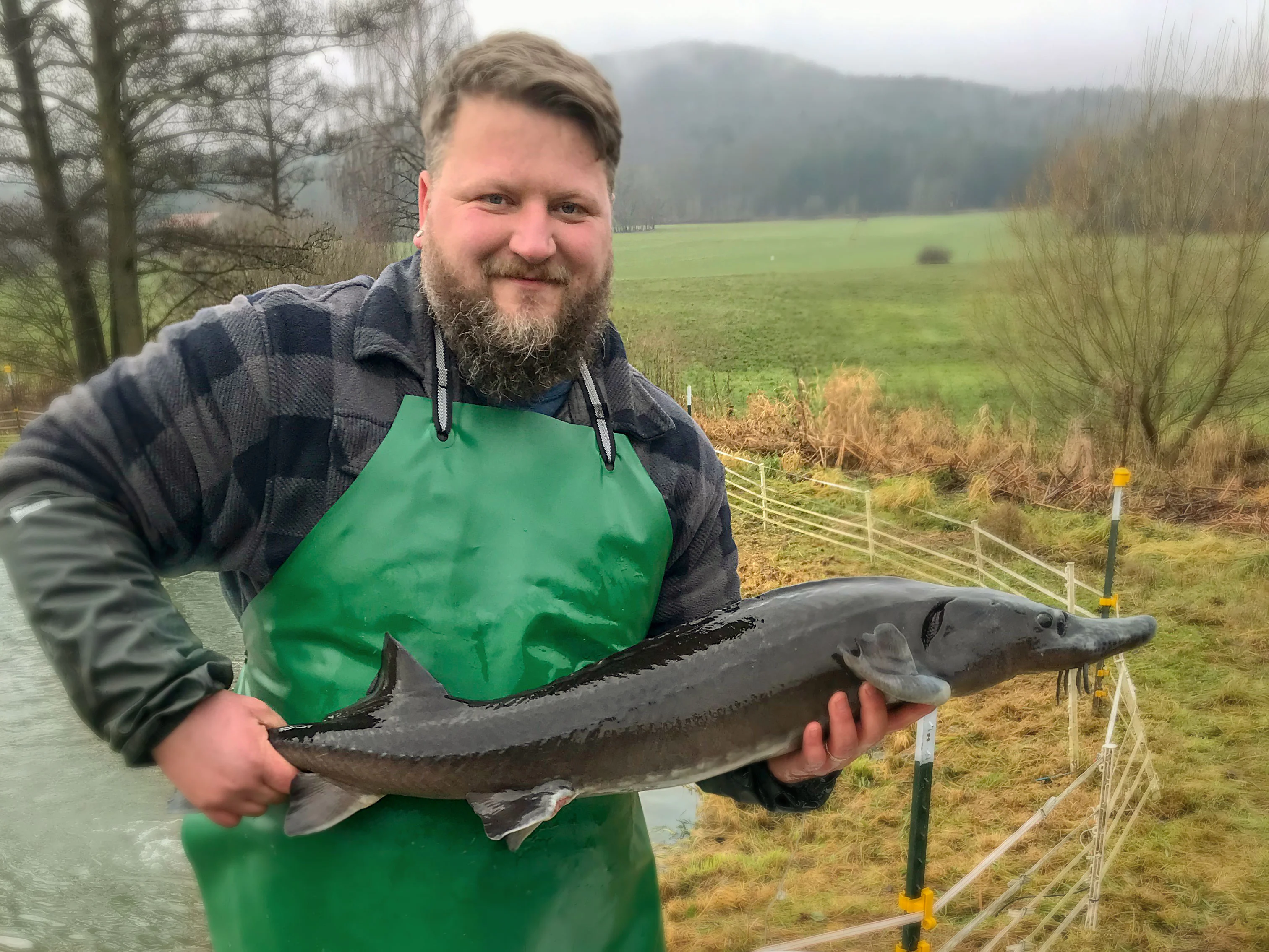 Potraitaufnahme von Thomas Nürnberger mit einem langen Fisch in beiden Händen und der Natur im Hintergrund