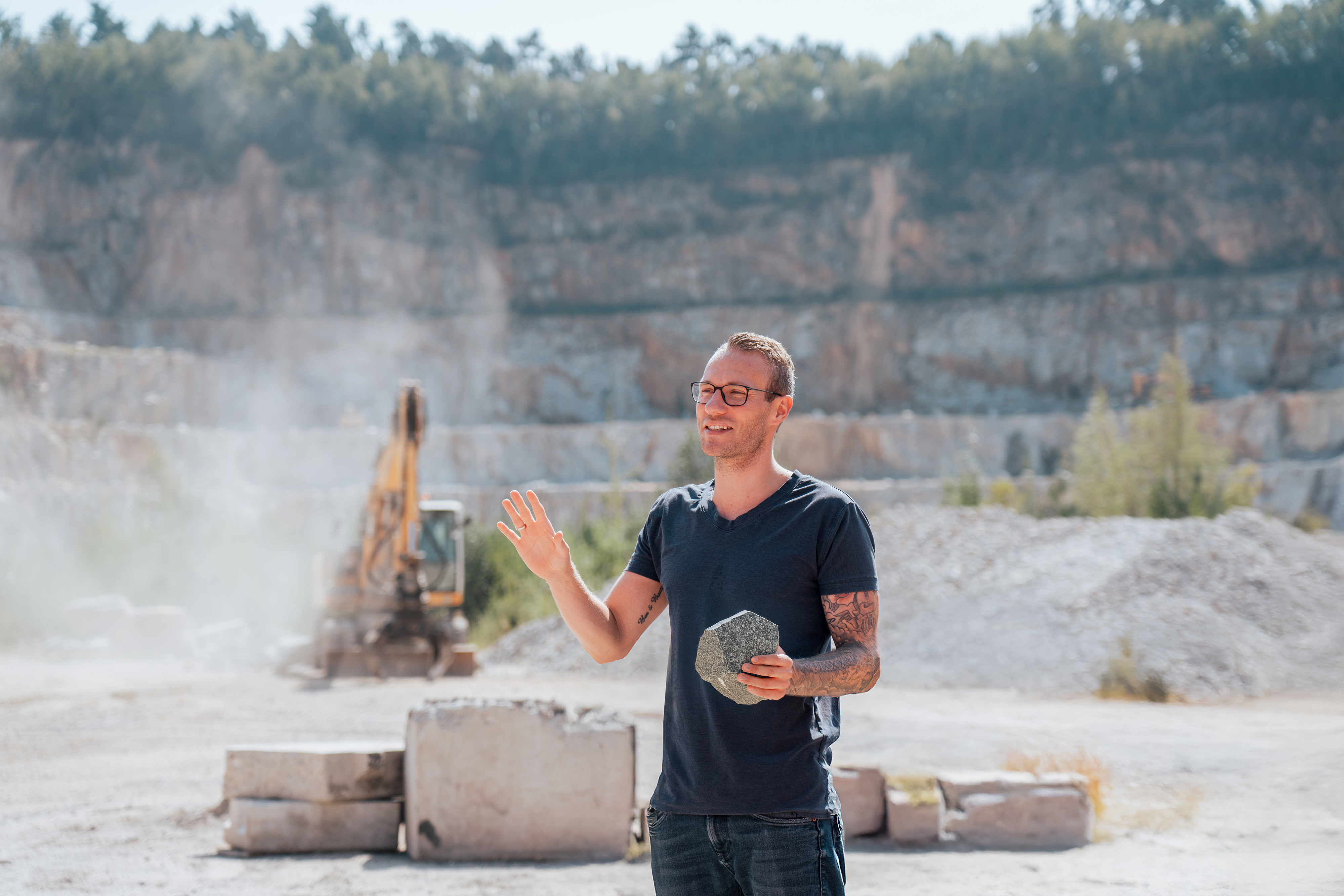 Jeremias Geißler, Betriebsleiter Steinbruch Blauberg, mit einem Granitstein in der Hand, im Hintergrund der Steinbruch und ein Bagger