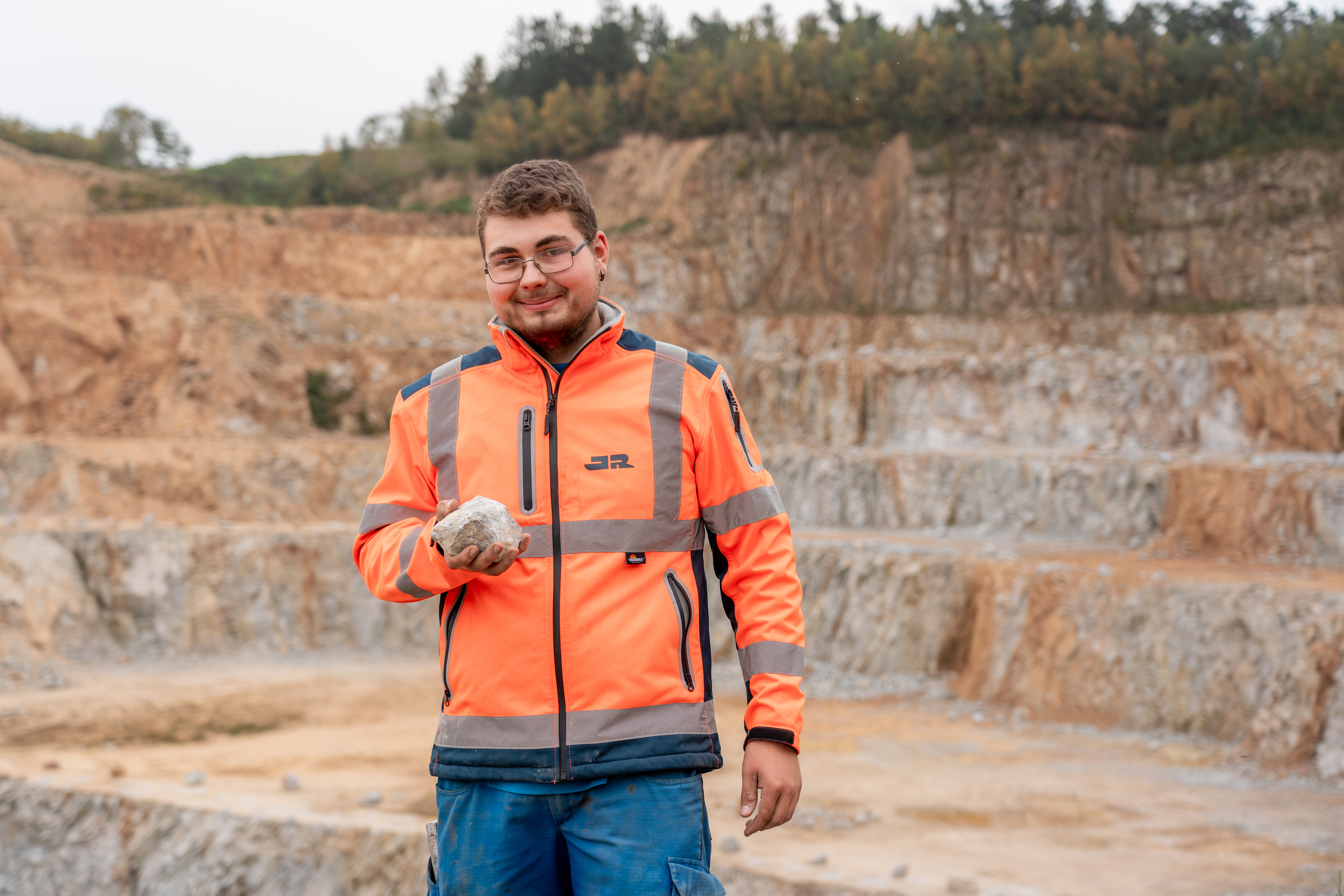 Jonas Freimuth steht im Steinbruch und hält einen Stein in der Hand