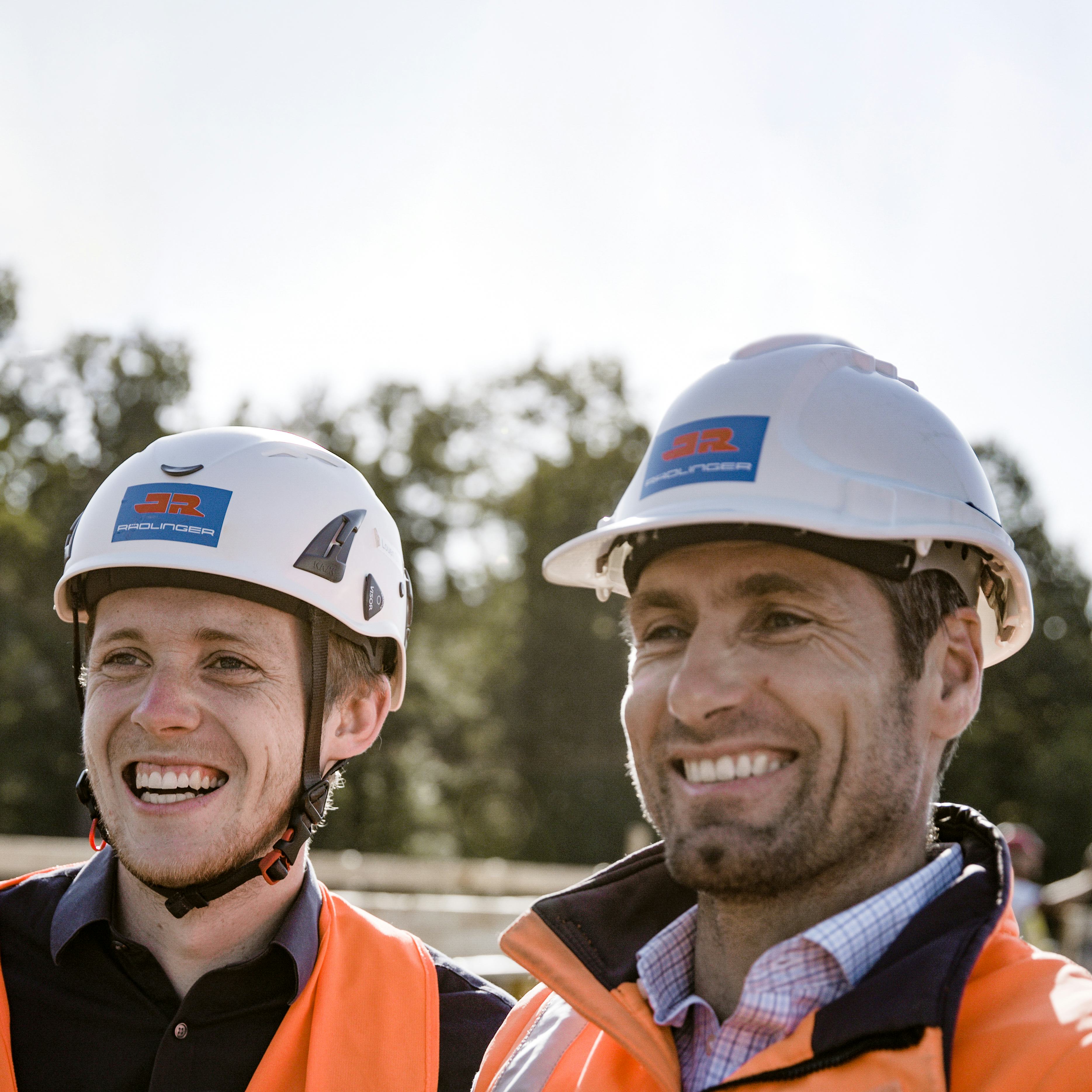 Zwei Bauleiter mit Bauhelm lächelnd auf der Baustelle, Detailaufnahme