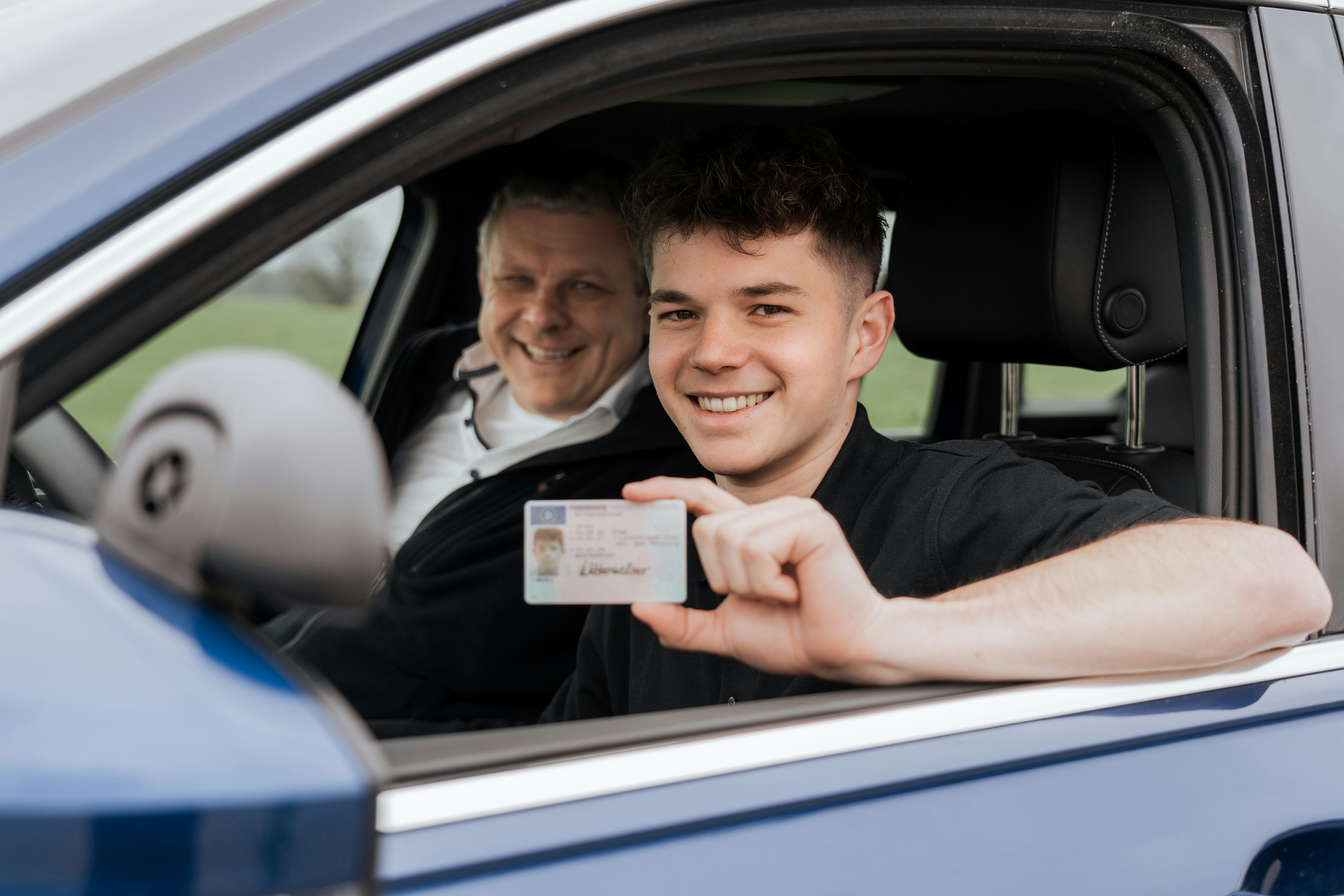 Azubi mit Fahrlehrer im Fahrschulauto der JR Verkehrsakademie, Azubi hält Führerschein in der Hand
