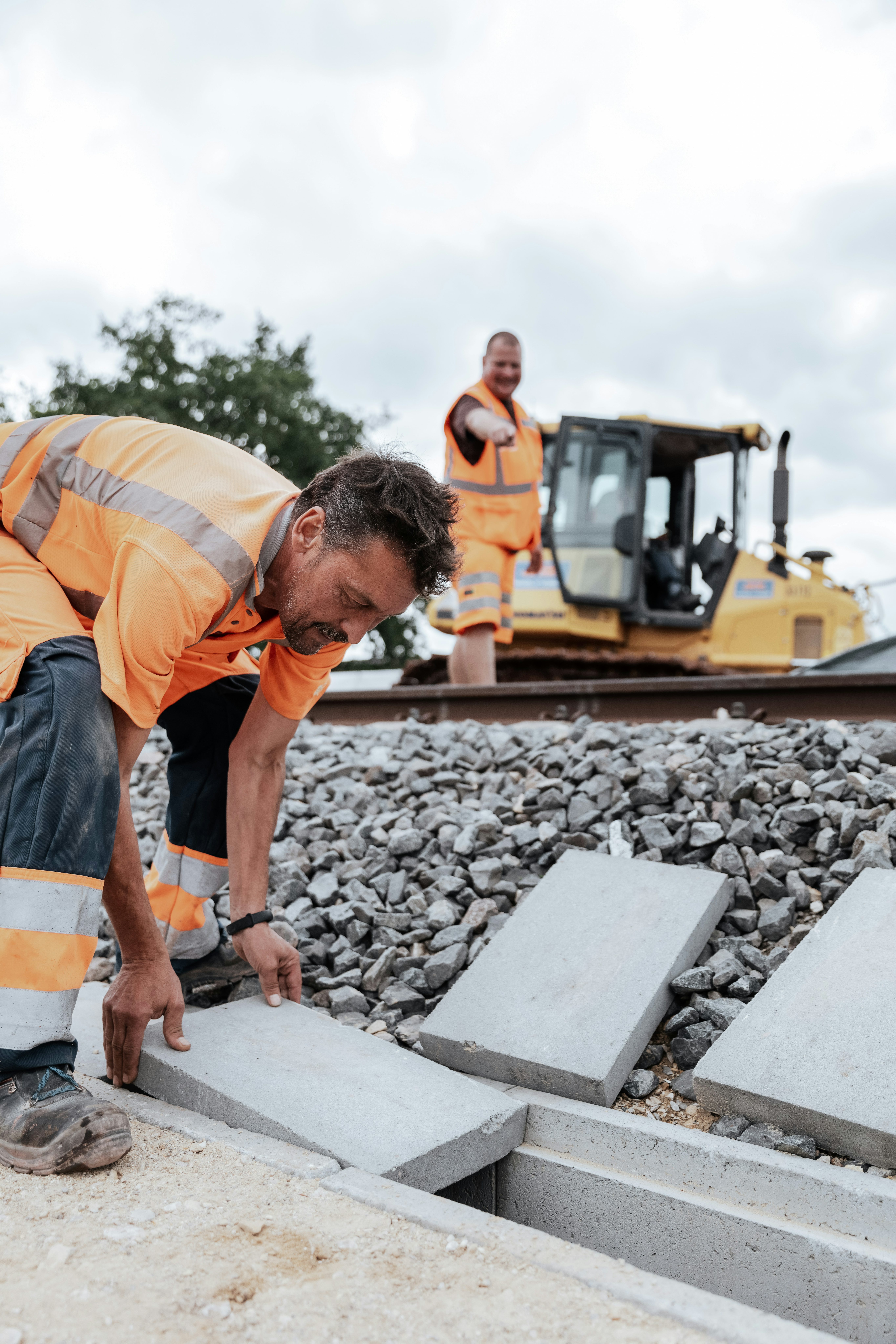Bauarbeiter verlegt Betonplatten auf einer Baustelle neben einem Schotterbett entlang einer Bahnstrecke