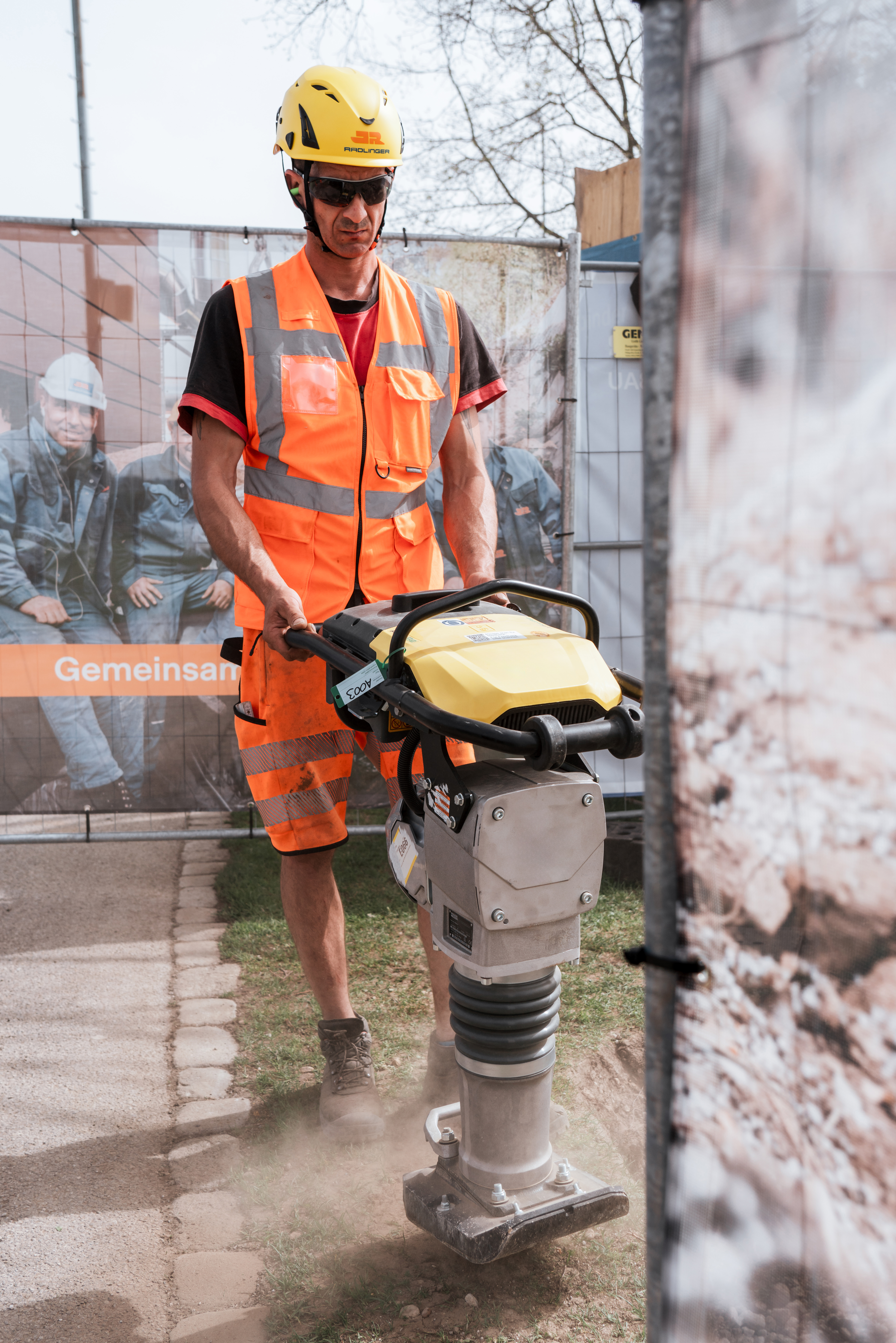 Bauarbeiter rüttelt mit E-Stampfer Boden auf einer Baustelle