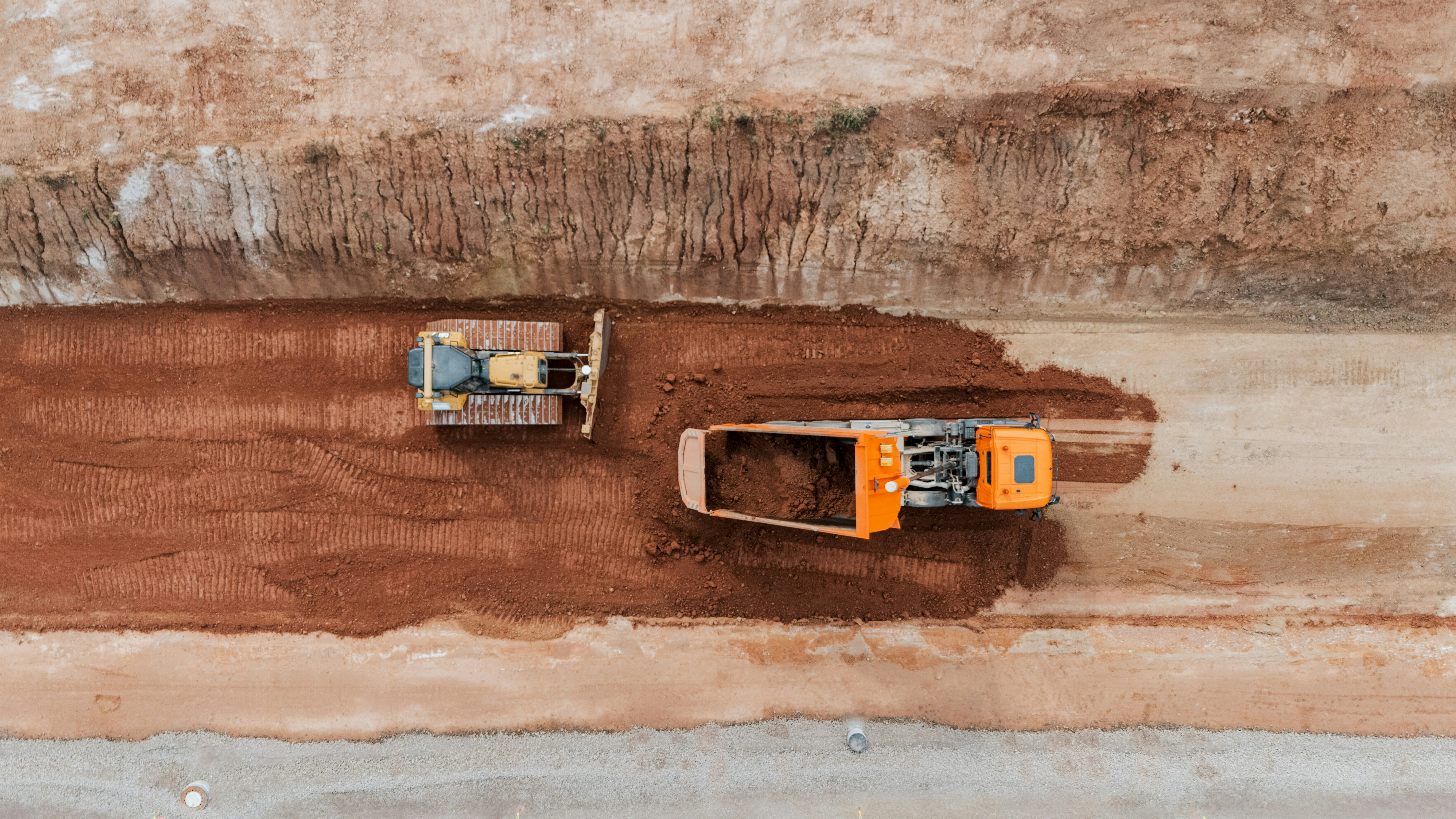 Raupe und Lkw bei Erdbauarbeiten auf einer Baustelle von oben