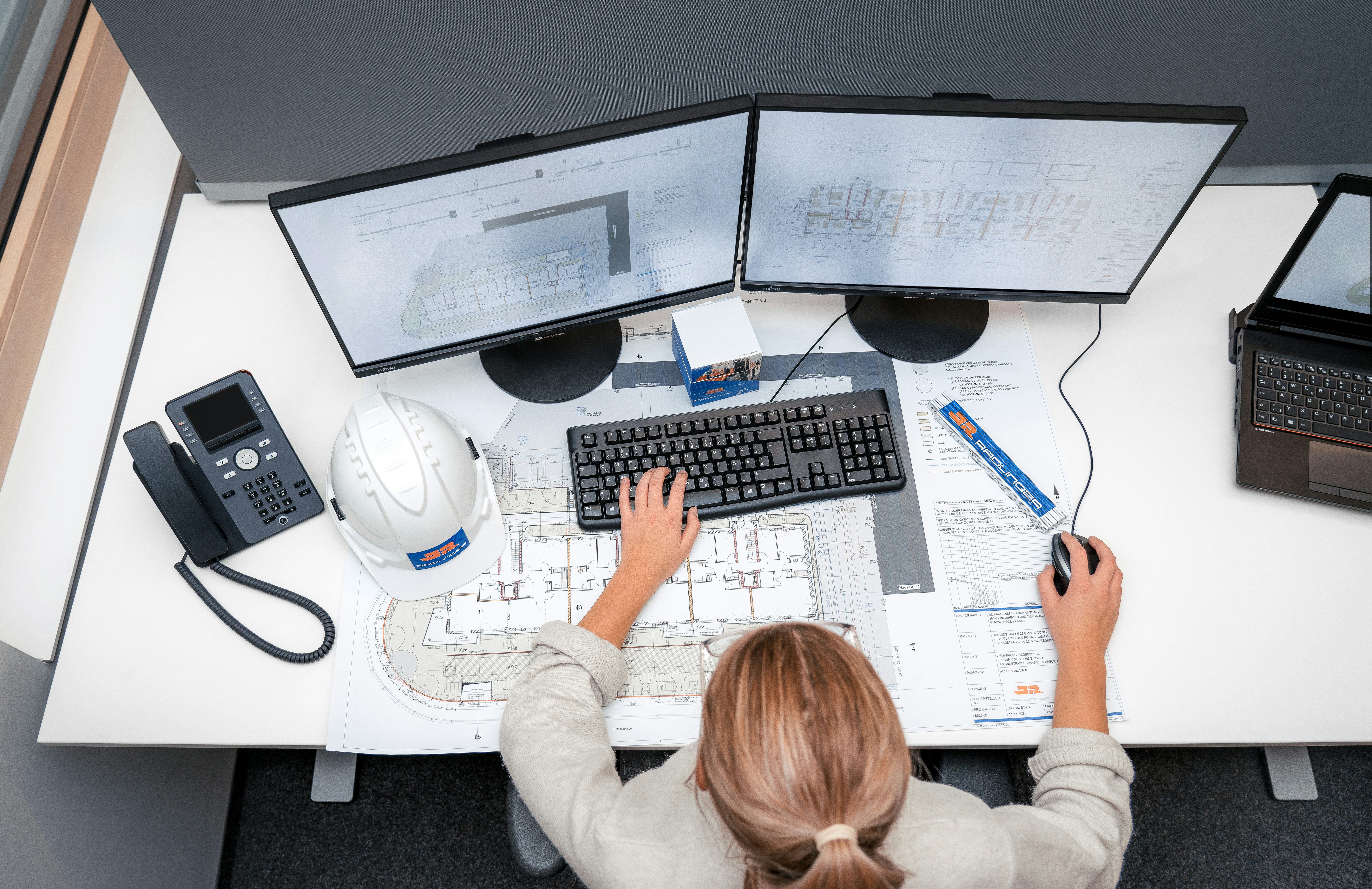 Büromitarbeitern mit Plänen vor PC, Draufsicht