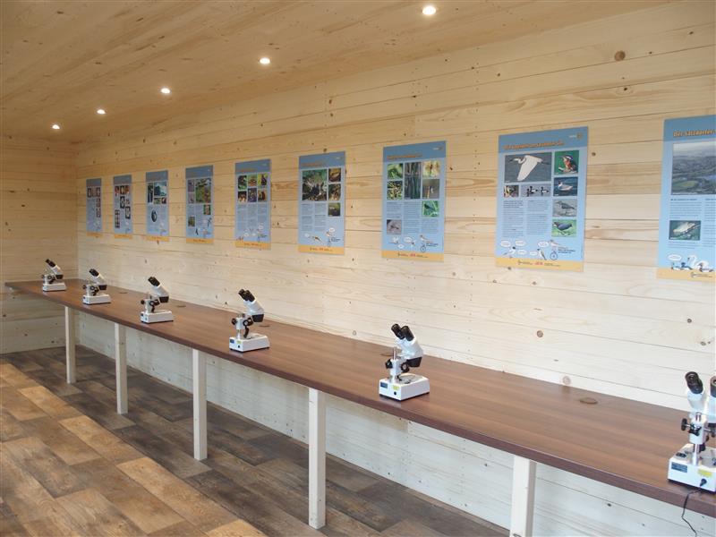 Naturkundelabor am Satzdorfer See: Raum mit Holzwänden, Mikroskopen auf langen Tischen und wissenschaftlichen Postern an der Wand