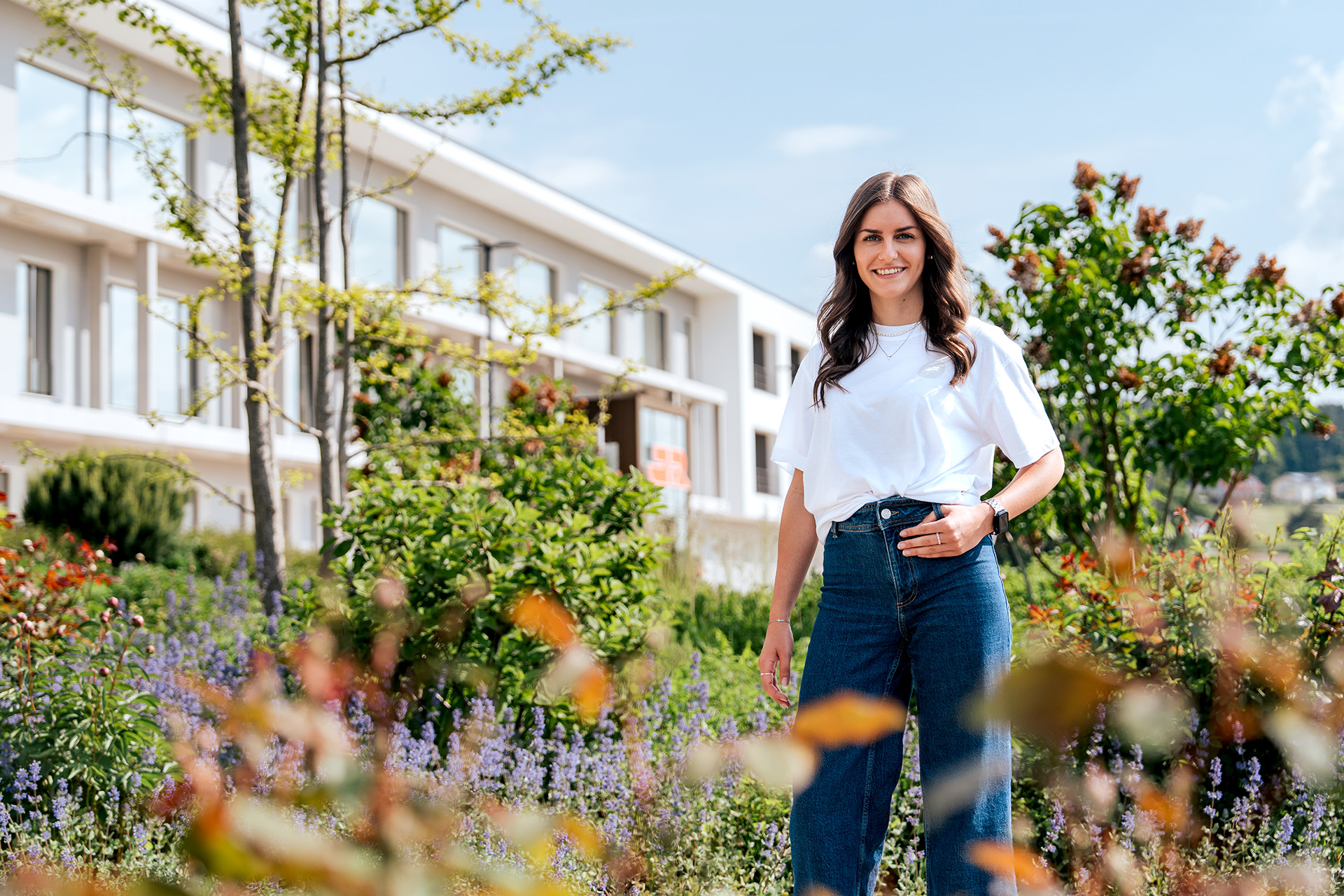 Bauzeichnerin Theresa Mühlbauer steht in dem blühenden Firmengarten vor der Hauptverwaltung in Cham und lächelt in die Kamera