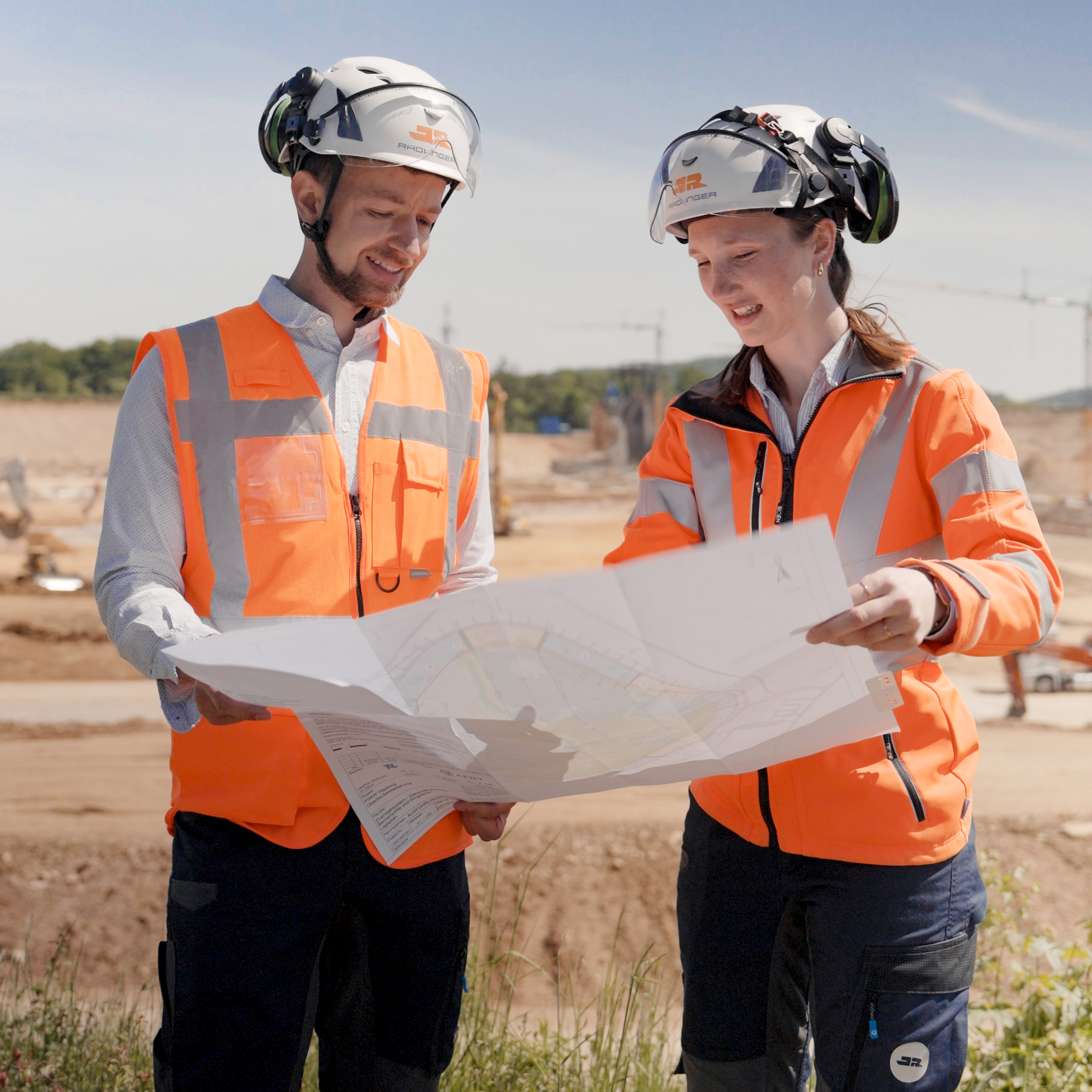 Bauleiter und Bauleiterin mit Bauplan auf einer Baustelle