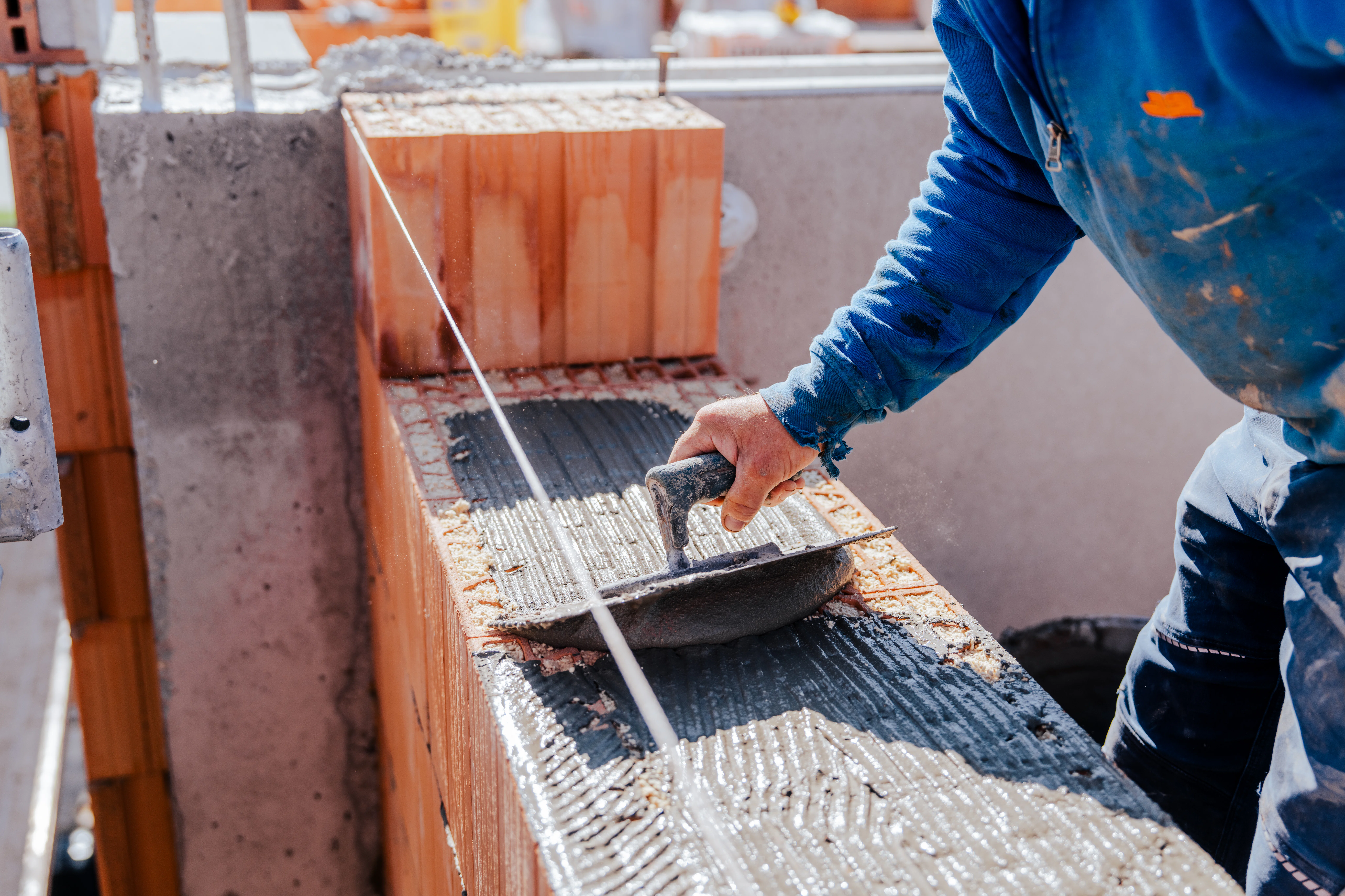 Ein Mitarbeitender trägt Spachtelmasse auf die Ziegel auf