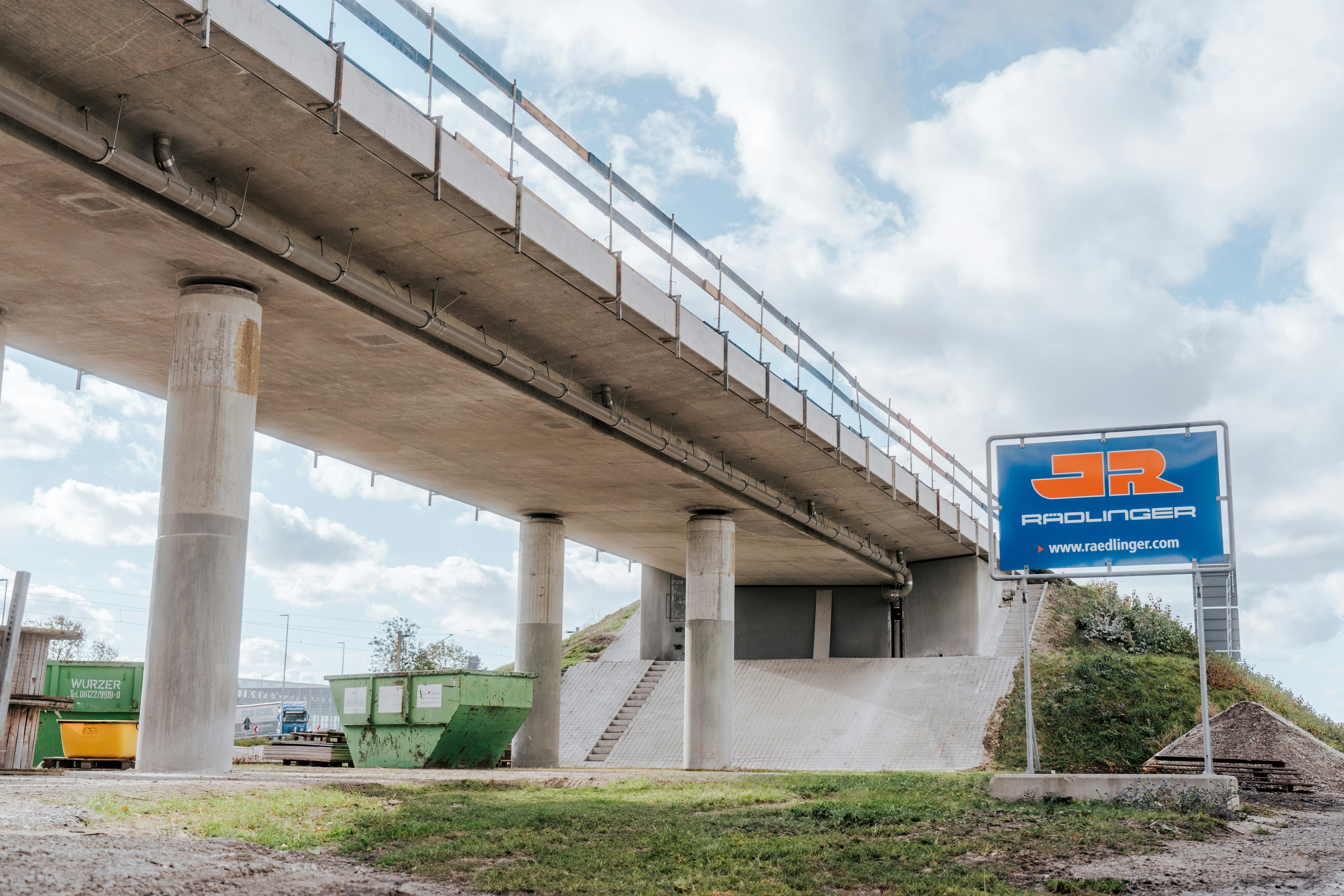 Sanierung der Straßenbrücke Knoten-West am Flughafen München: Brücke mit Bautafel der Josef Rädlinger Unternehmensgruppe
