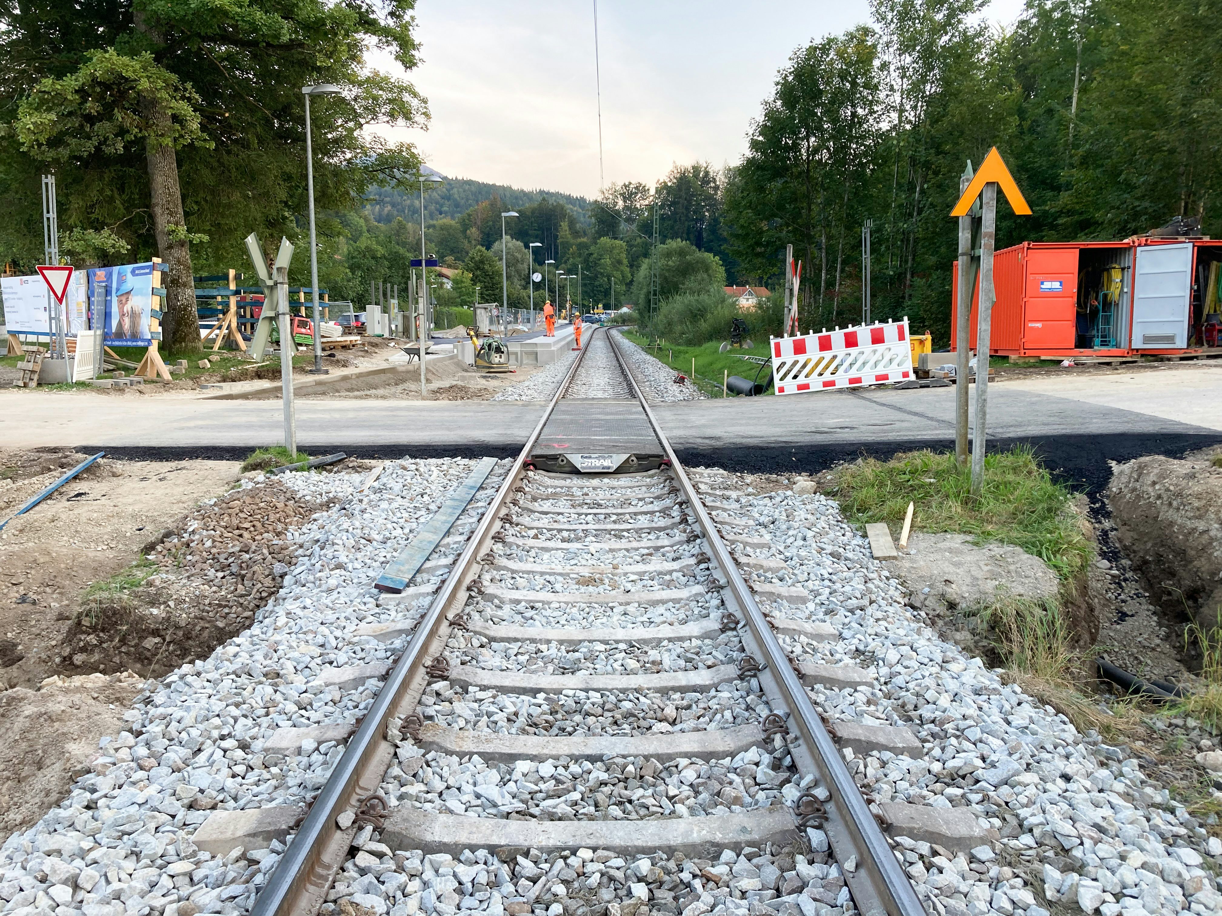 Frisch asphaltierter Bahnübergang, im Hintergrund: Neu gepflasterter Haltepunkt