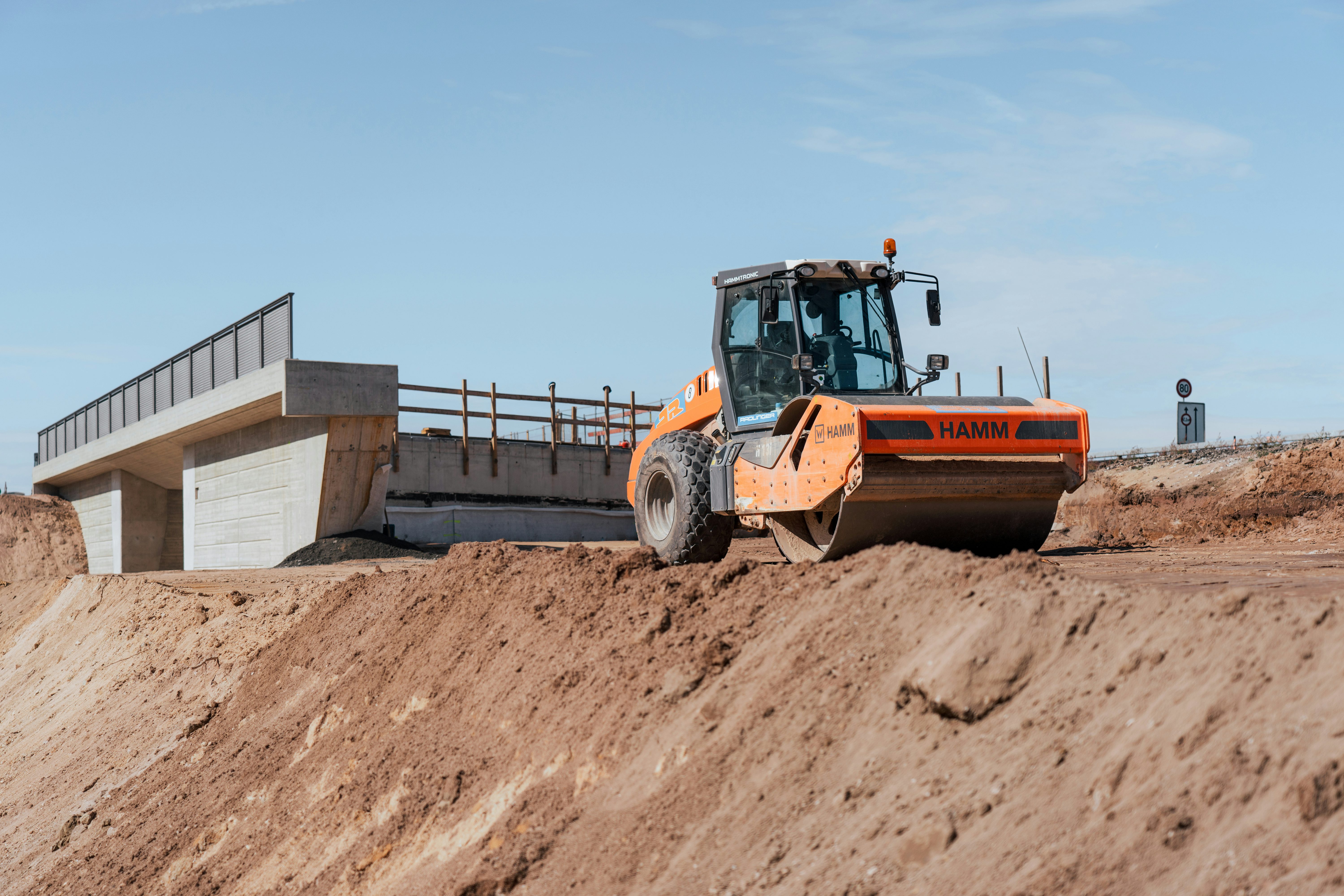 Asphaltfräsguts: Walze befestigt Boden, im Hintergrund Brücke im Bau