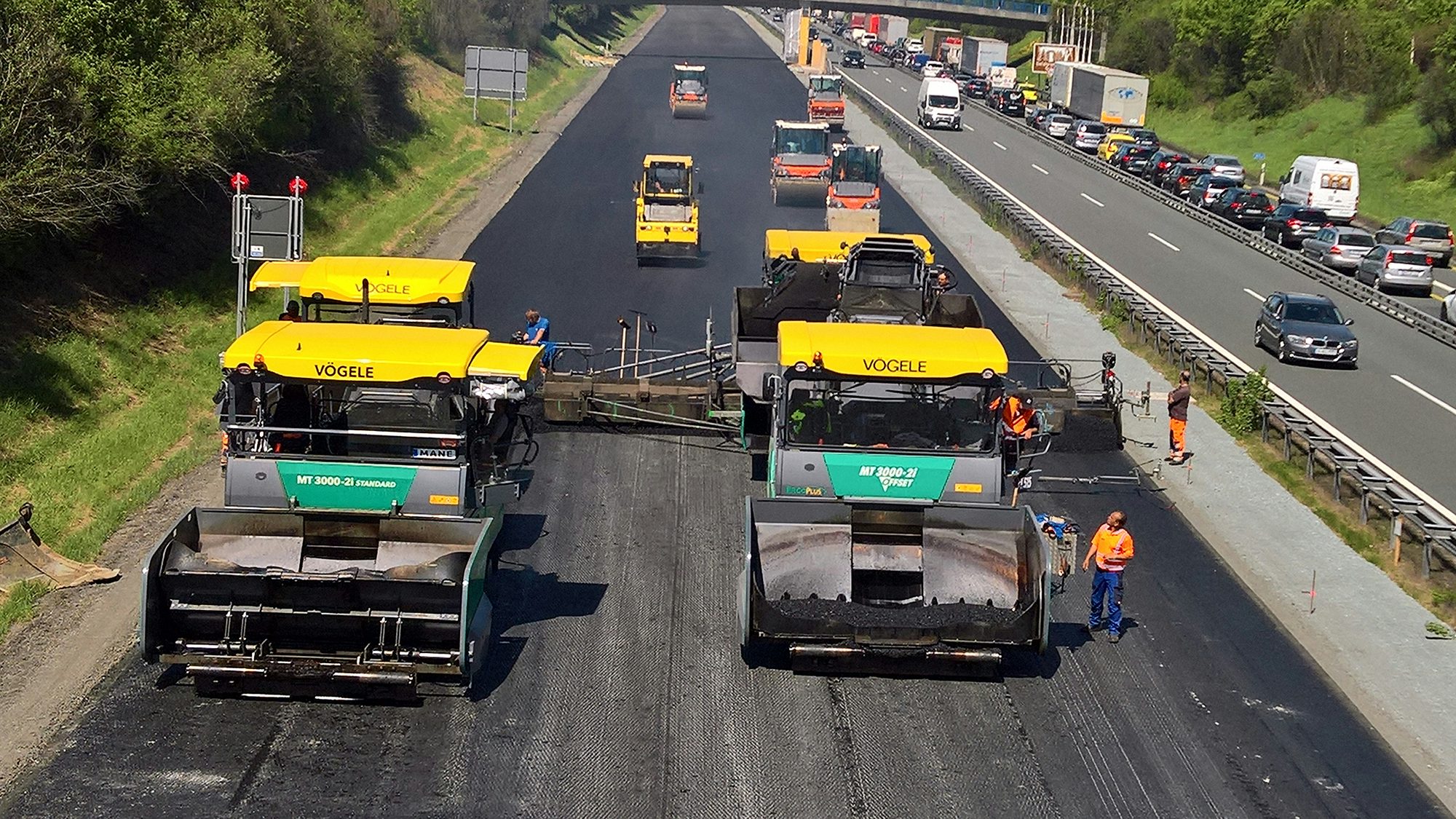 A9: Zwei Teermaschinen bei der Arbeit, im Hintergrund mehrere Walzen