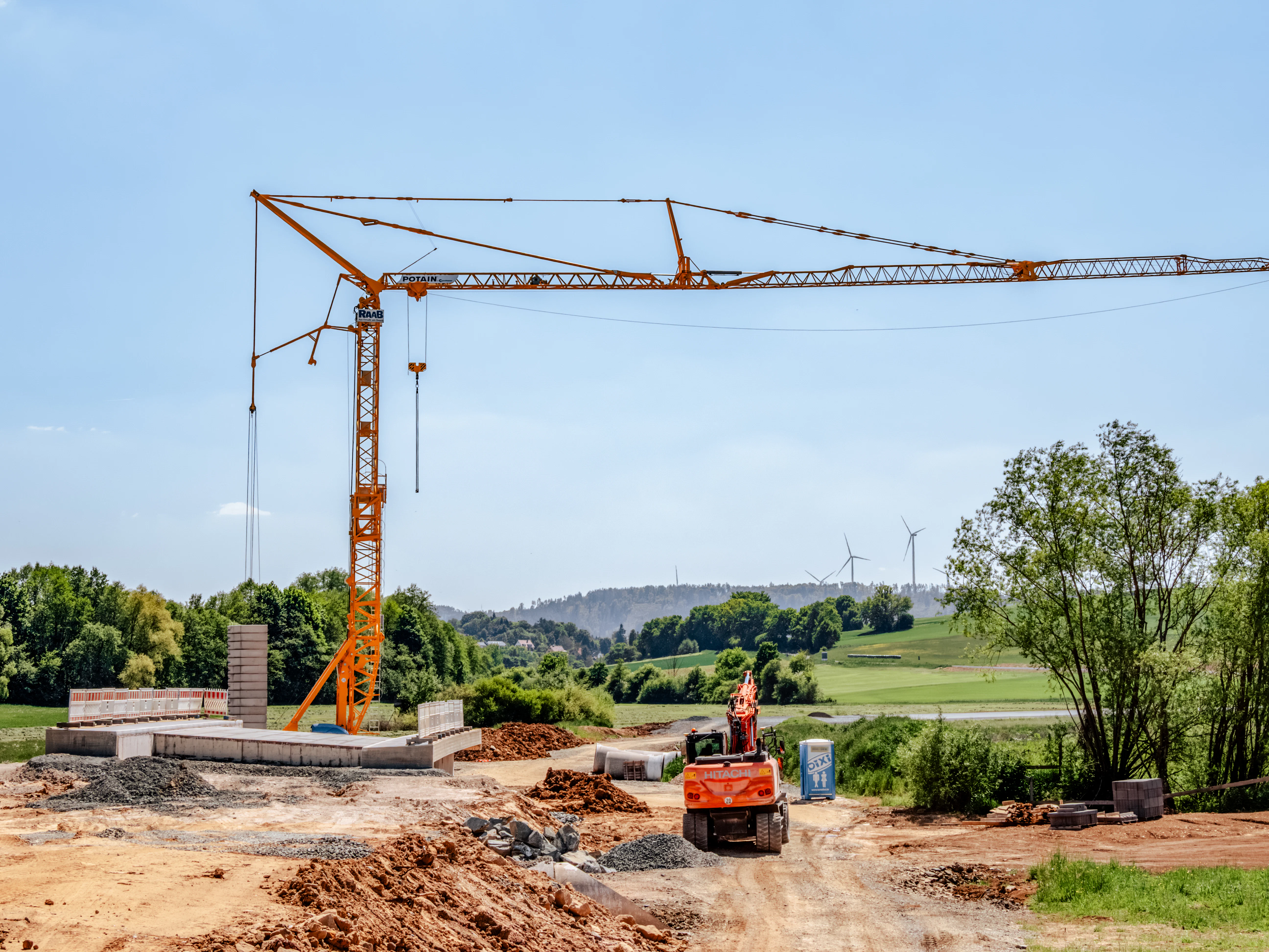 Baukran auf einer Baustelle mit Windrädern im Hintergrund und einem Bagger