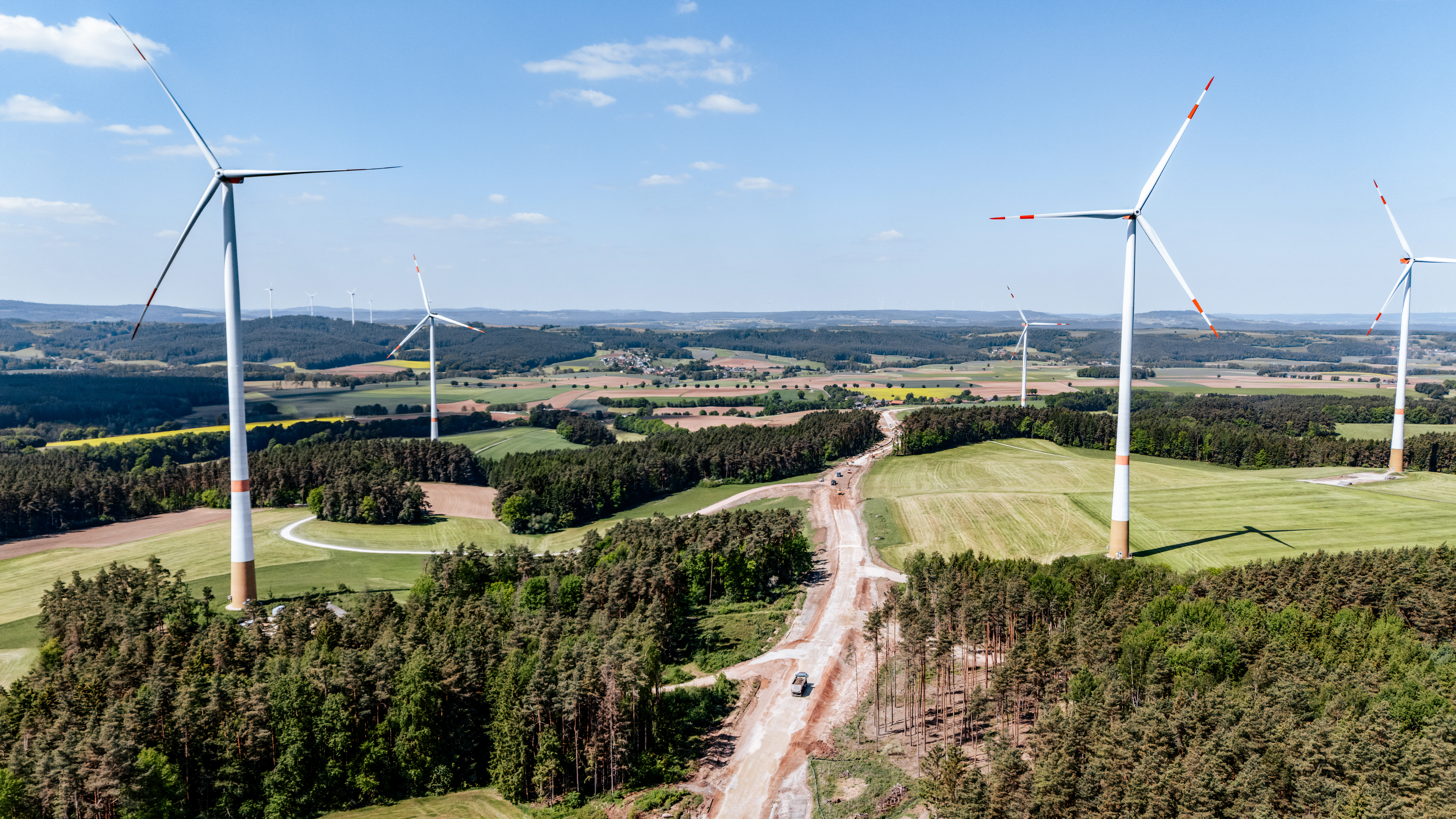 Drohnenaufnahme vieler Windräder, dazwischen verläuft eine Baustelle für eine Straße