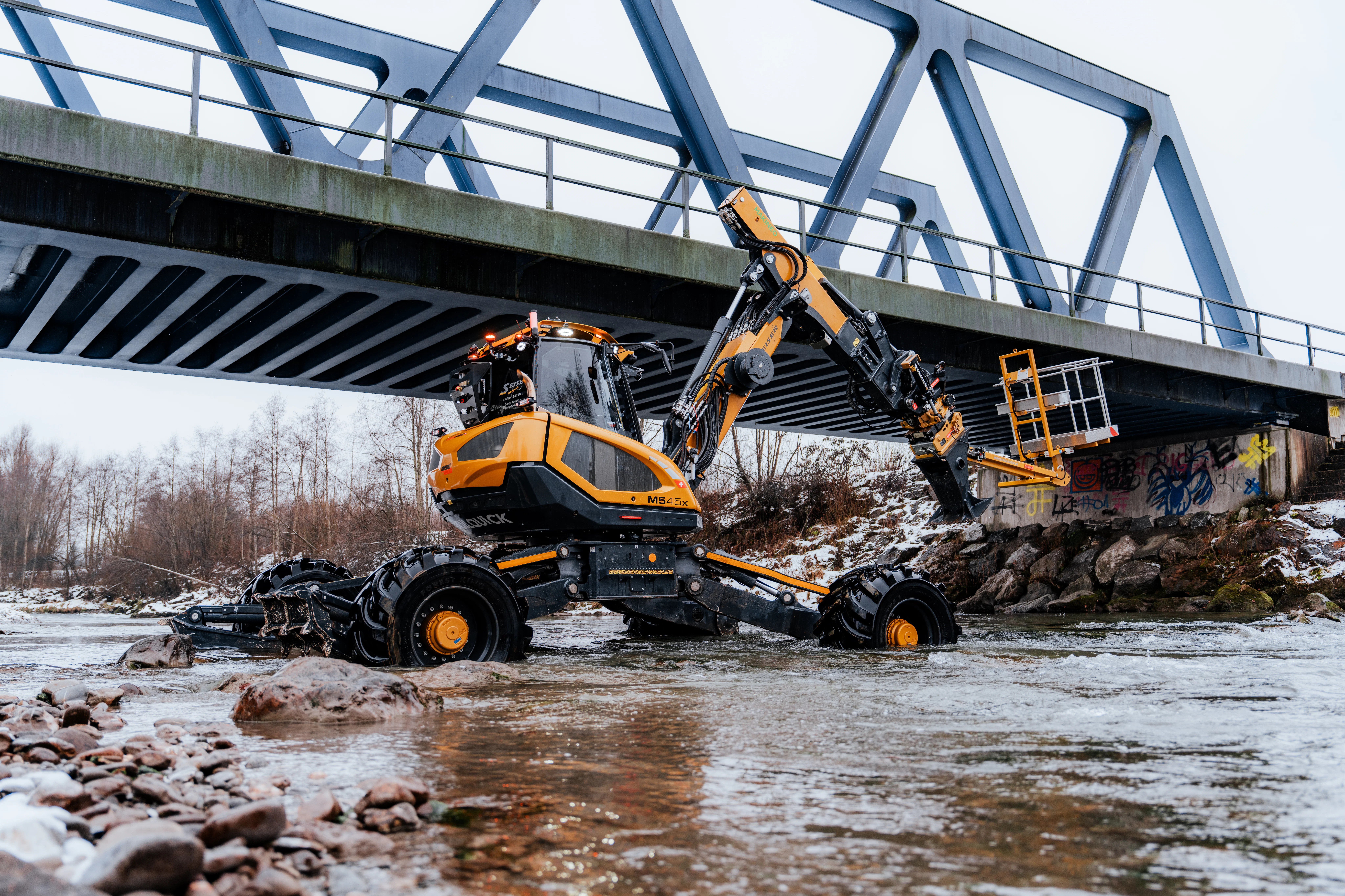 Schreitbagger im Fluss unter einer Brücke der Deutschen Bahn