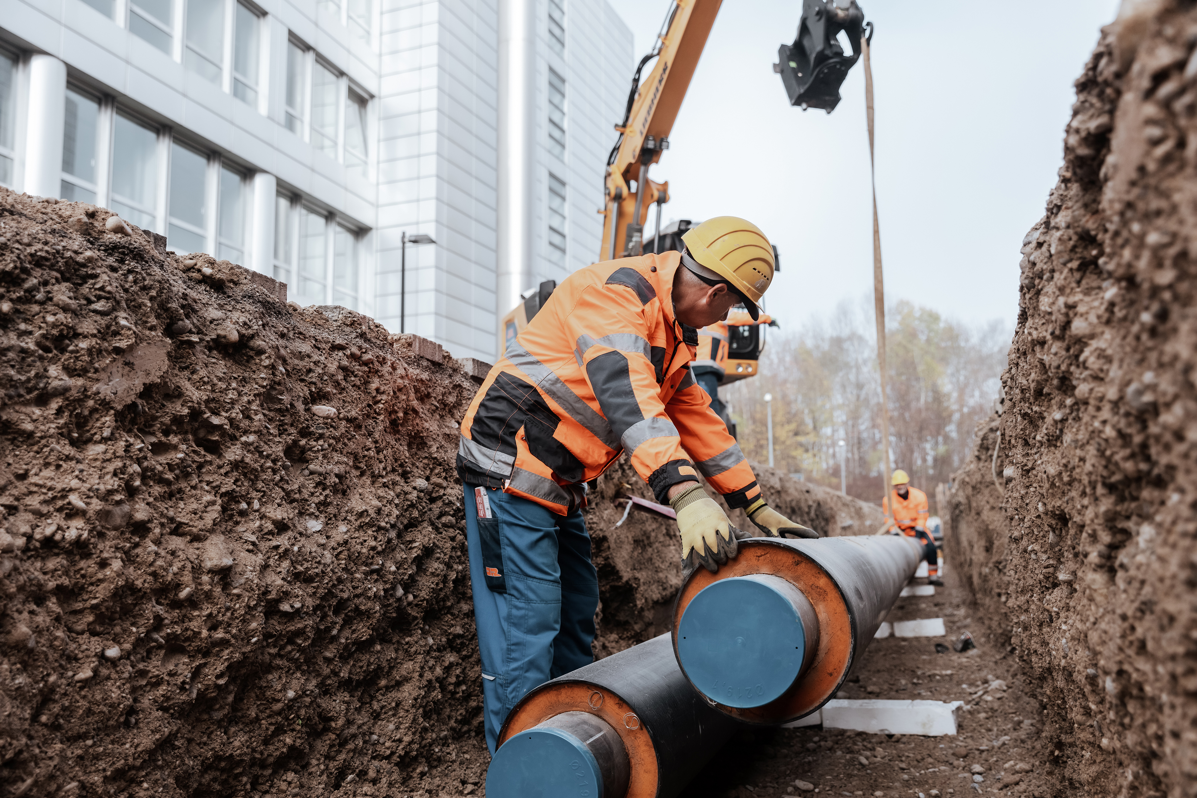 Rädlinger Mitarbeiter beim Einhub einer Fernwärmeleitung in einen Rohrgraben