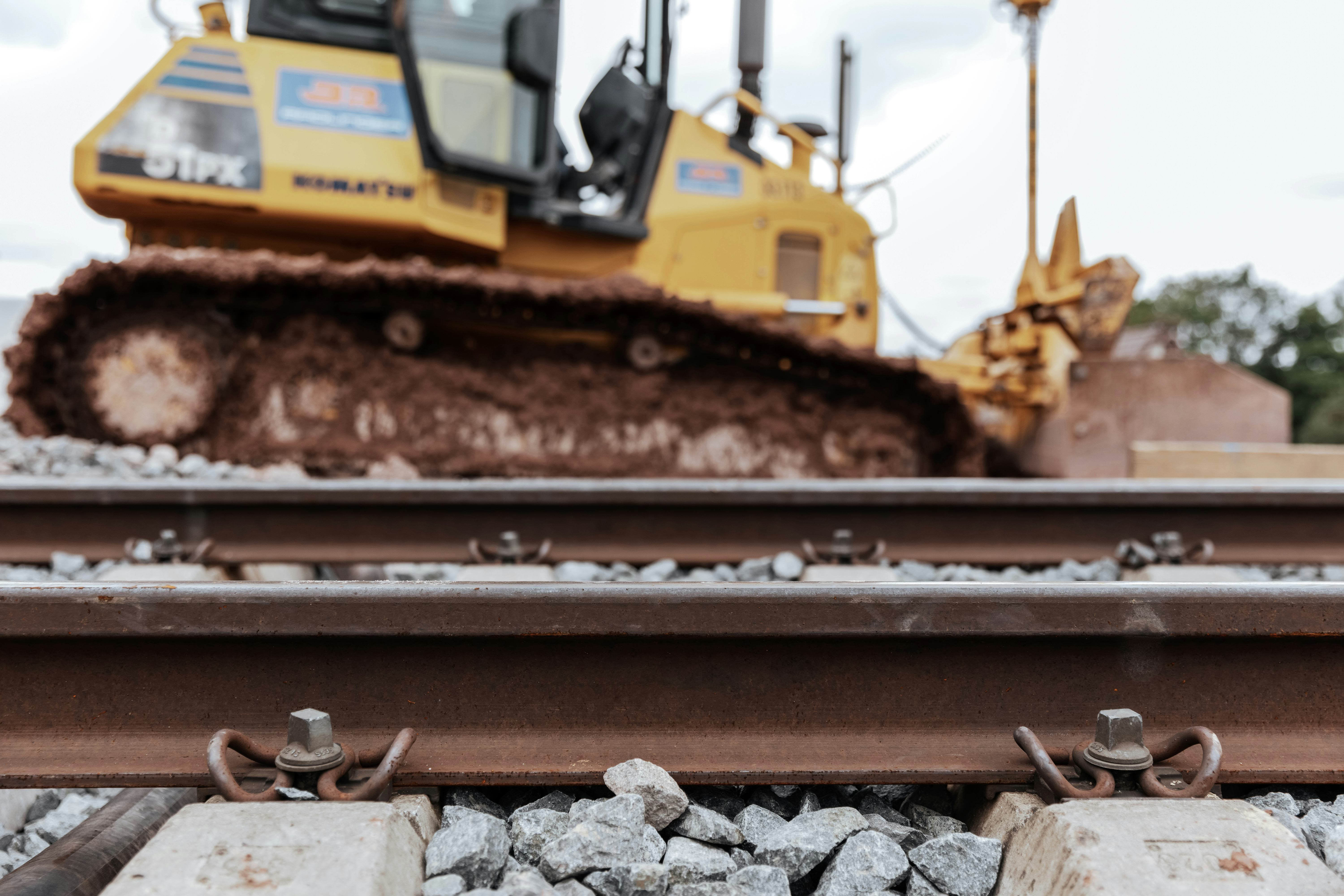 Detailaufnahme eines Bahngleises, im Hintergrund eine Raupe
