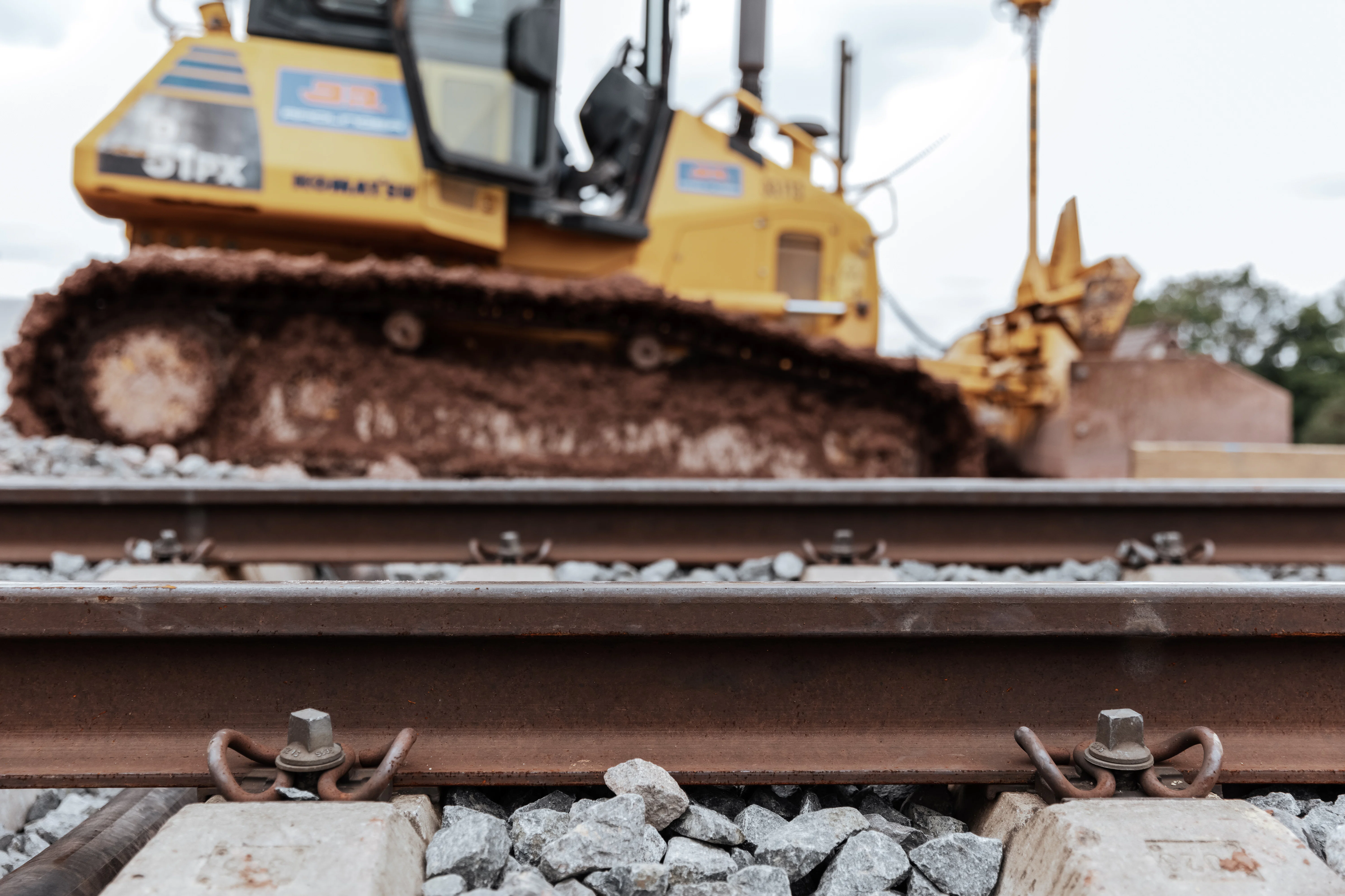 Detailaufnahme eines Bahngleises, im Hintergrund eine Raupe