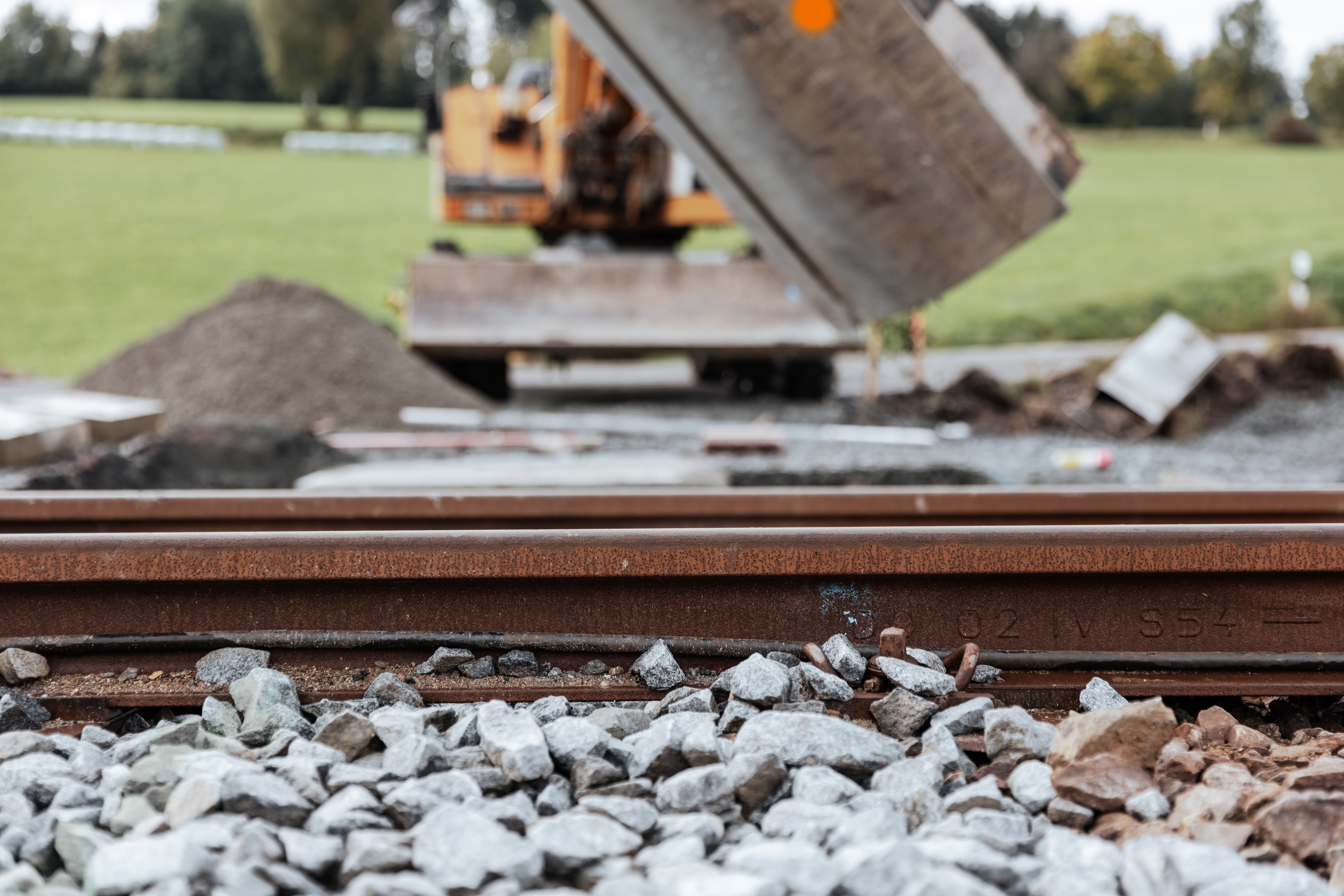 Detailaufnahme eines Bahngleises, im Hintergrund ein Bagger