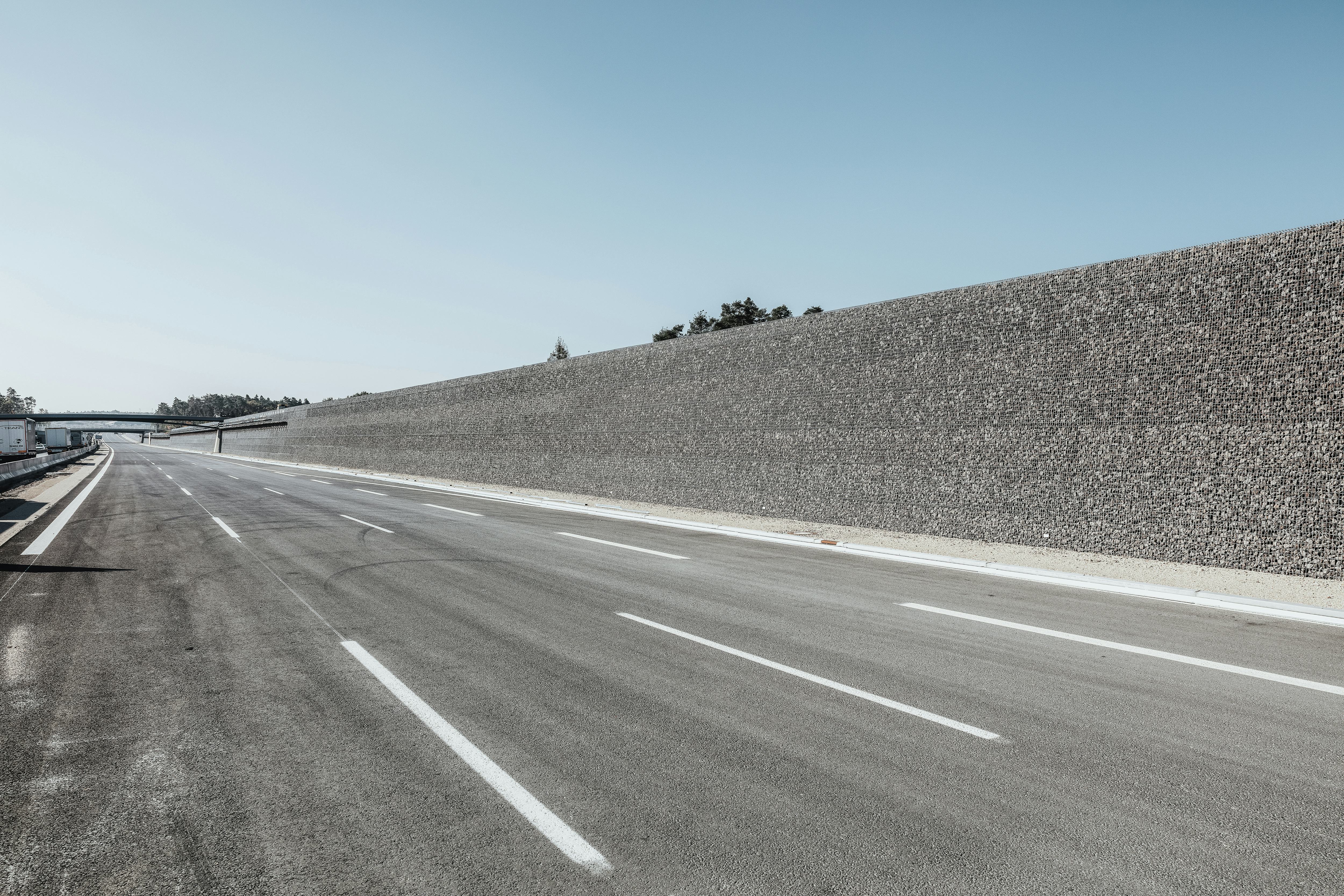Rädlinger Straßen- und Autobahnbau: Foto einer fertigen Straße mit zwei Brücken und Lärmschutzwall aus Steinen