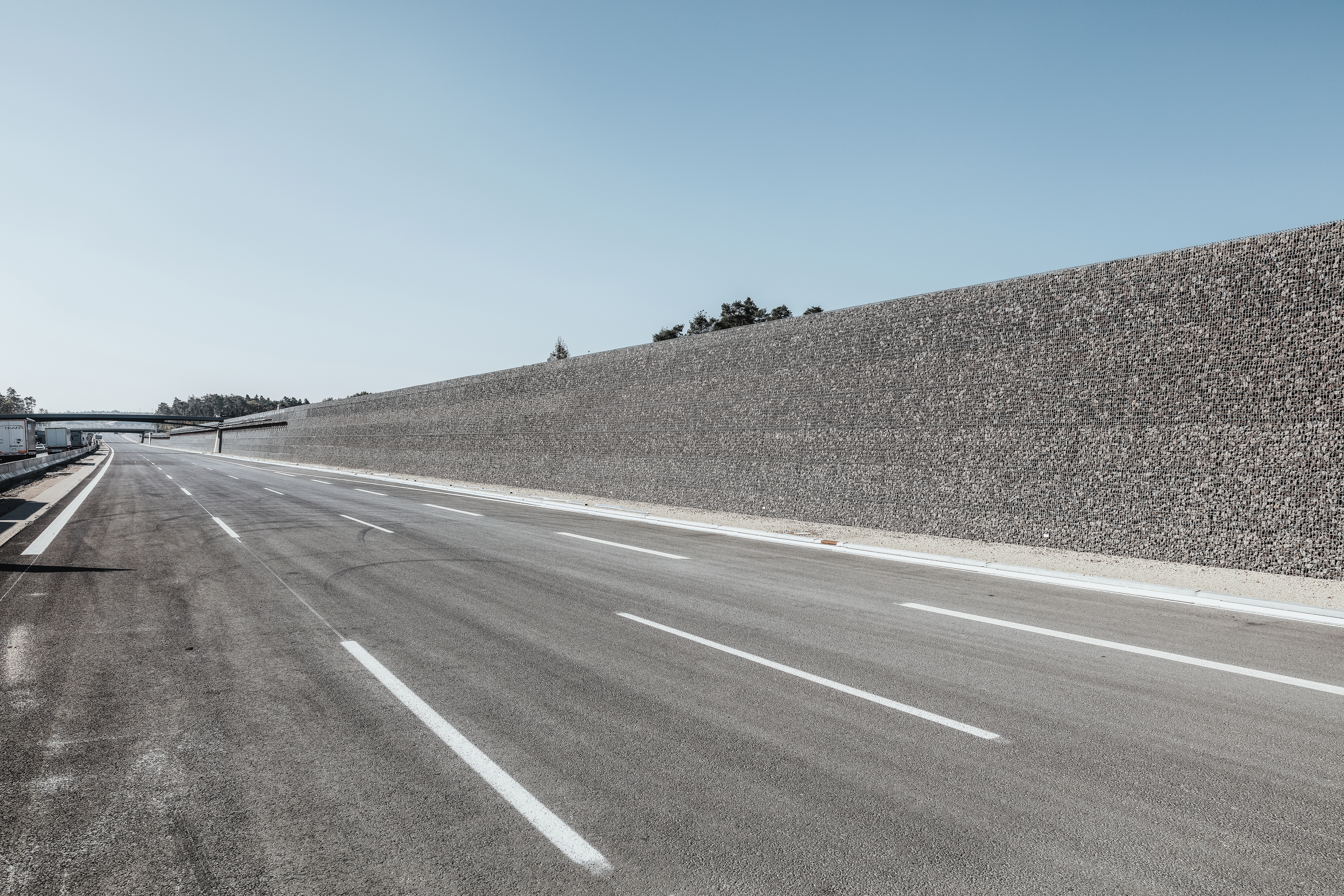 Rädlinger Straßen- und Autobahnbau: Foto einer fertigen Straße mit zwei Brücken und Lärmschutzwall aus Steinen