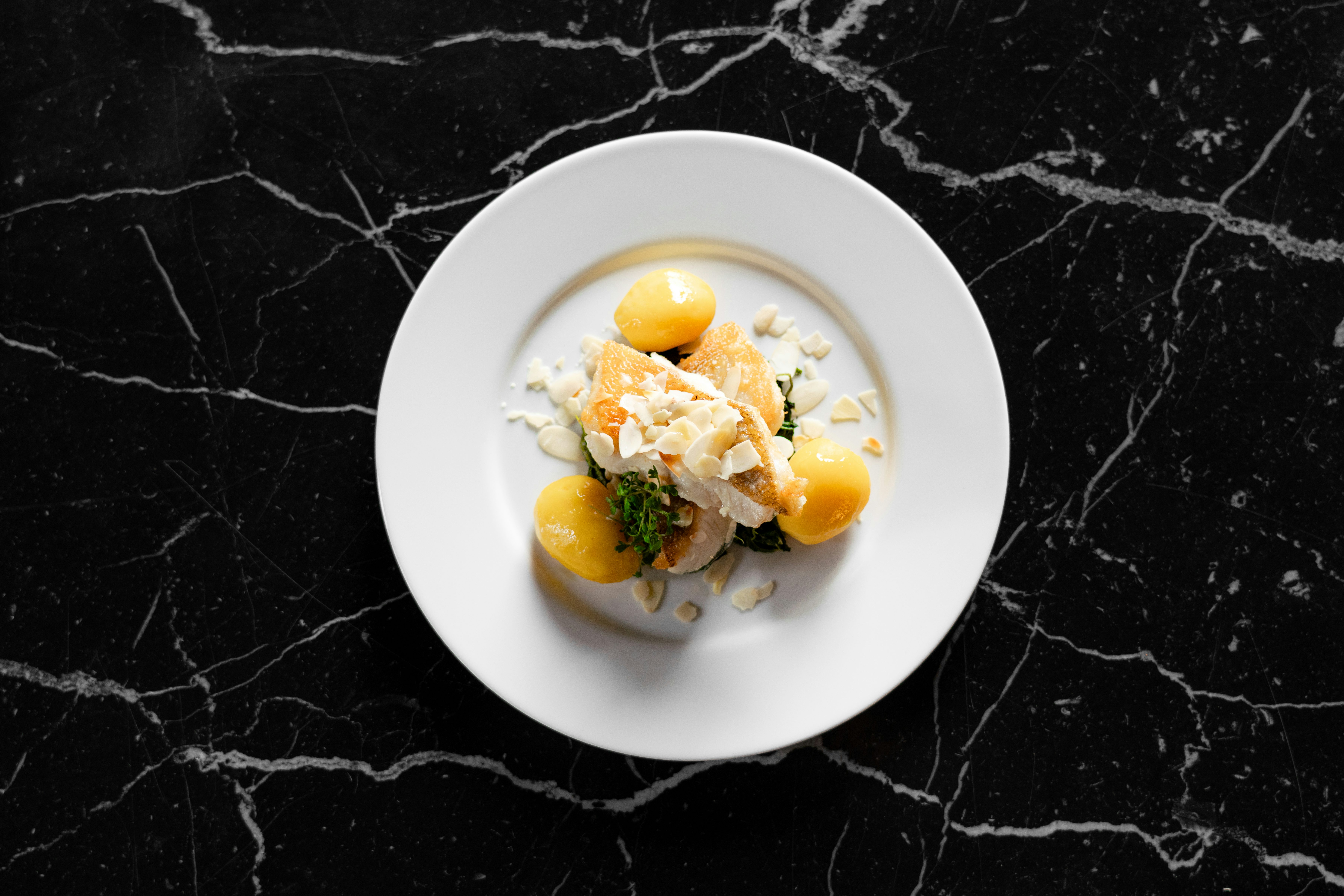 Gericht aus dem 's Kloster: Fischfilet mit Kartoffeln, Kräutern und Mandelblättchen angerichtet auf einem Teller