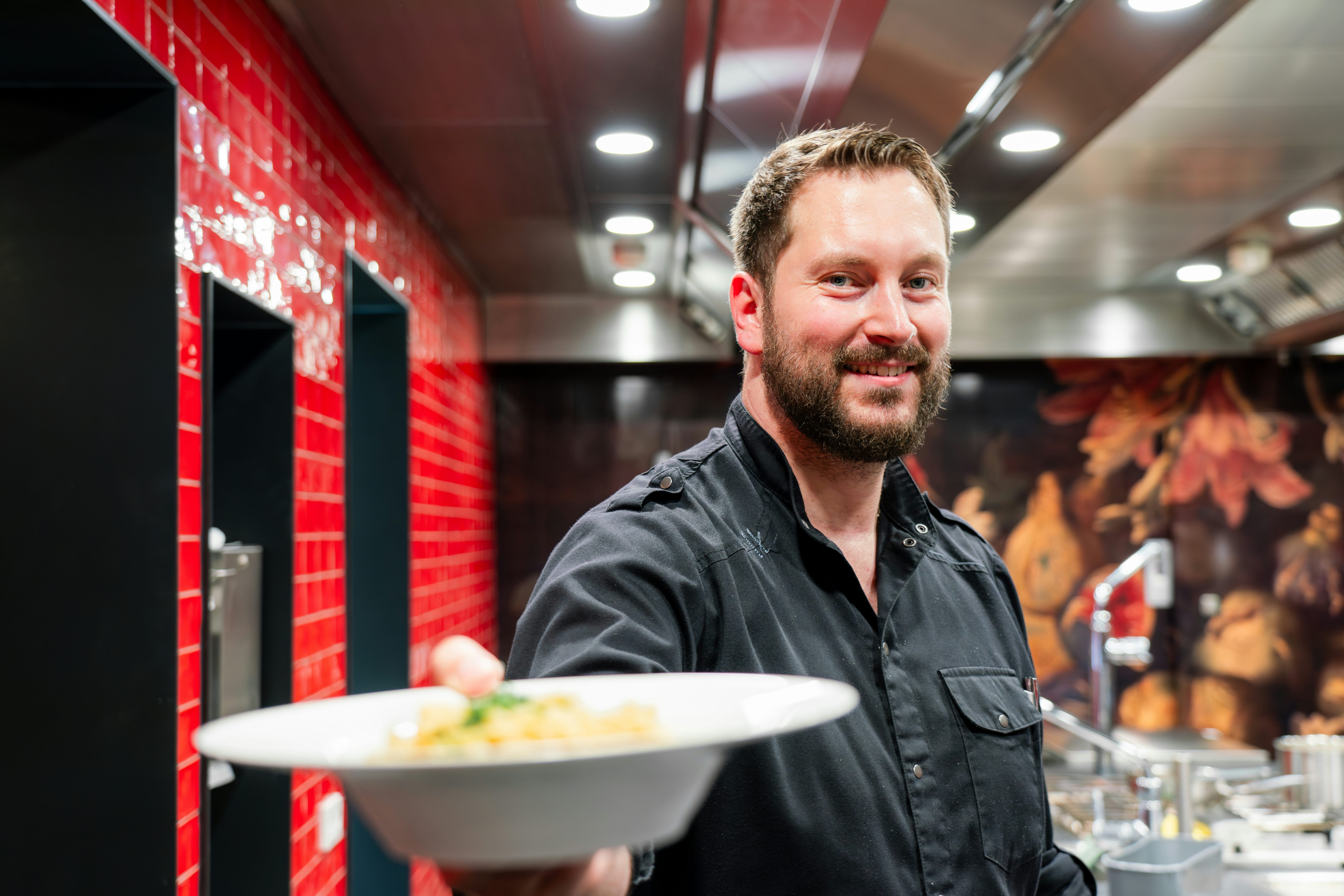 Koch im 's Kloster bei der Essensausgabe, in die Kamera lächelnd